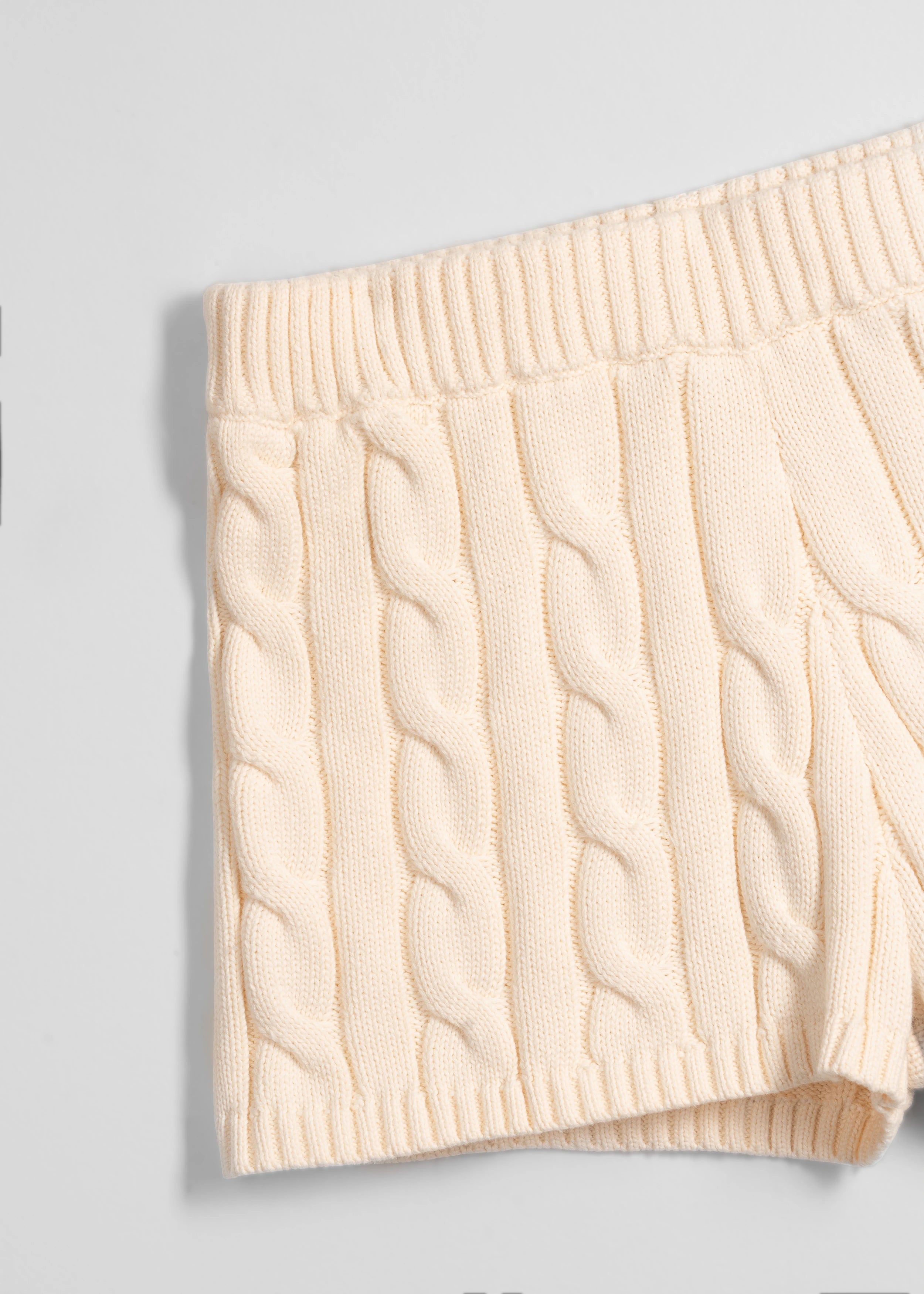 La Corsia Cable Knit Mini Short in cream, made from heavyweight cotton with a fitted silhouette, ribbed waistband, and chunky cable texture throughout.