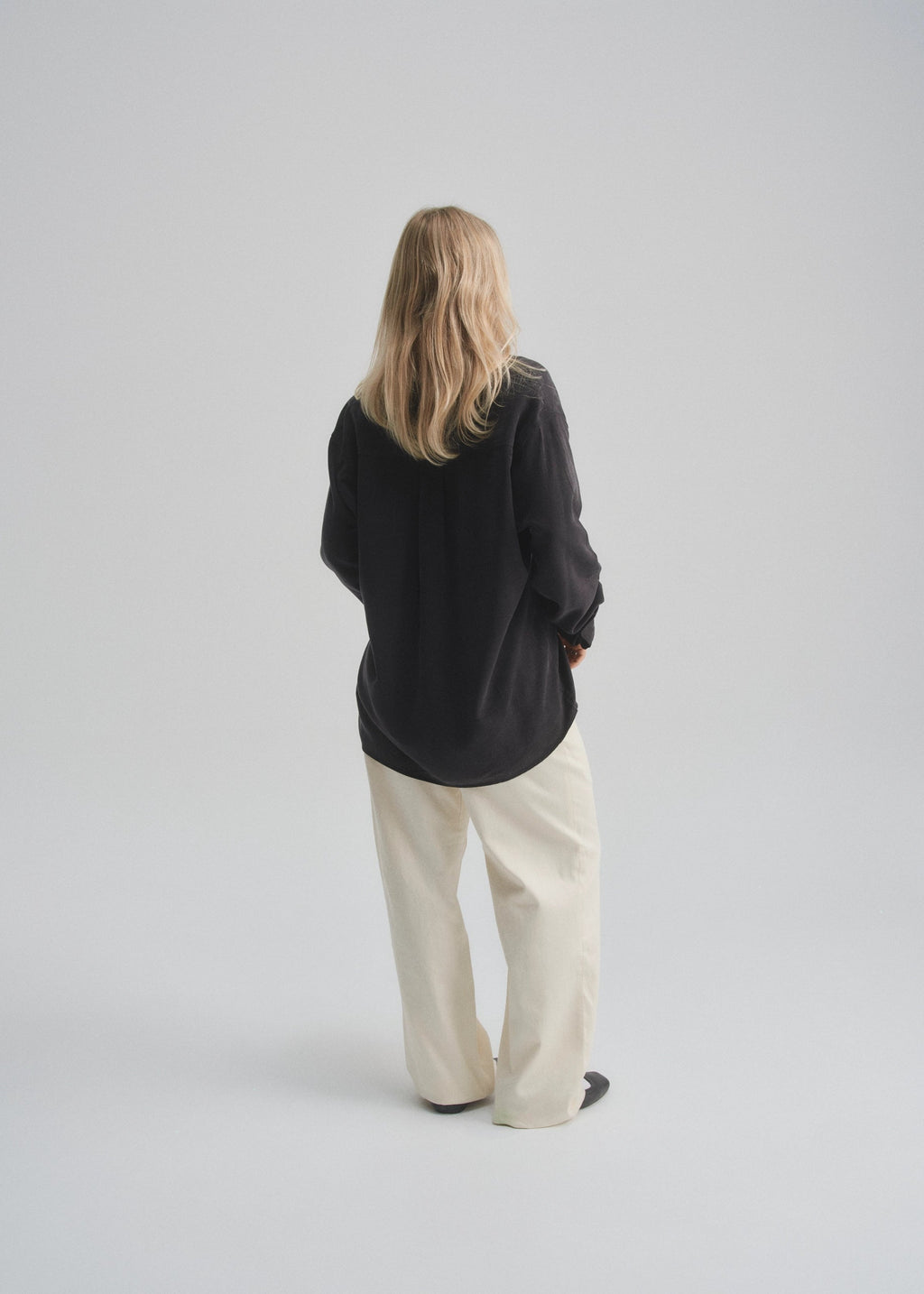 Model wearing a black button up shirt and cream pants on a plain background