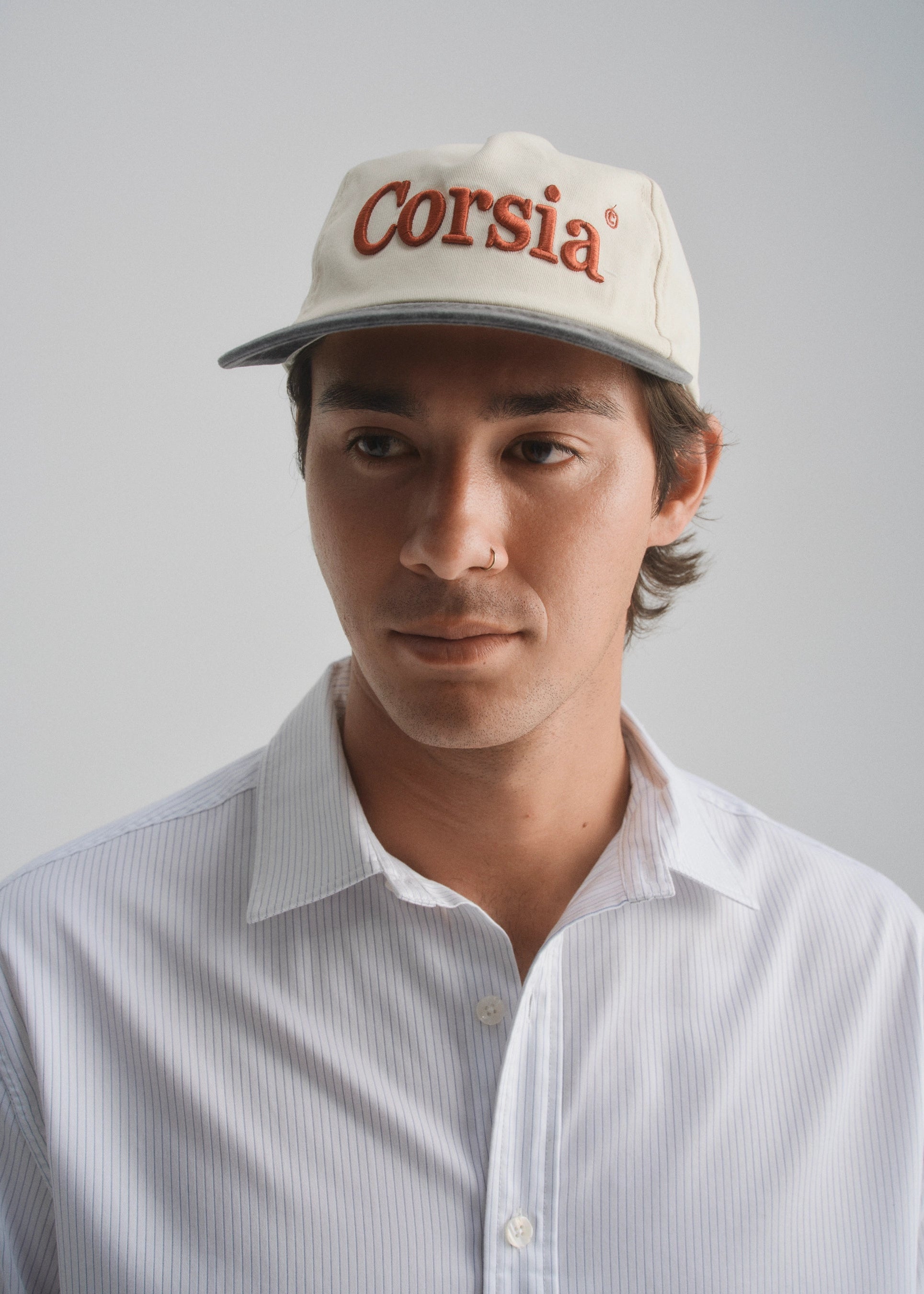 Man wearing a cap with 'Corsia' logo against a plain background