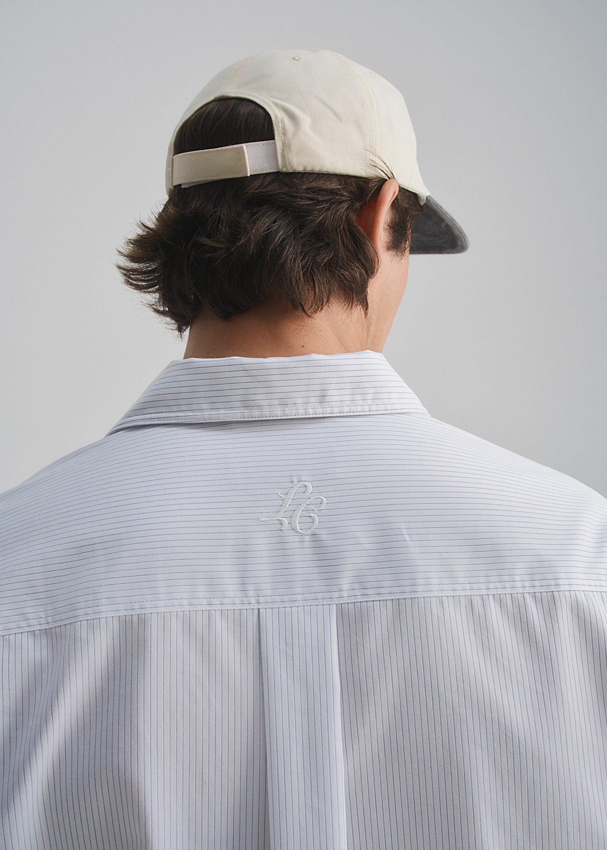 Person wearing a light-colored cap and striped shirt with a logo on a plain background