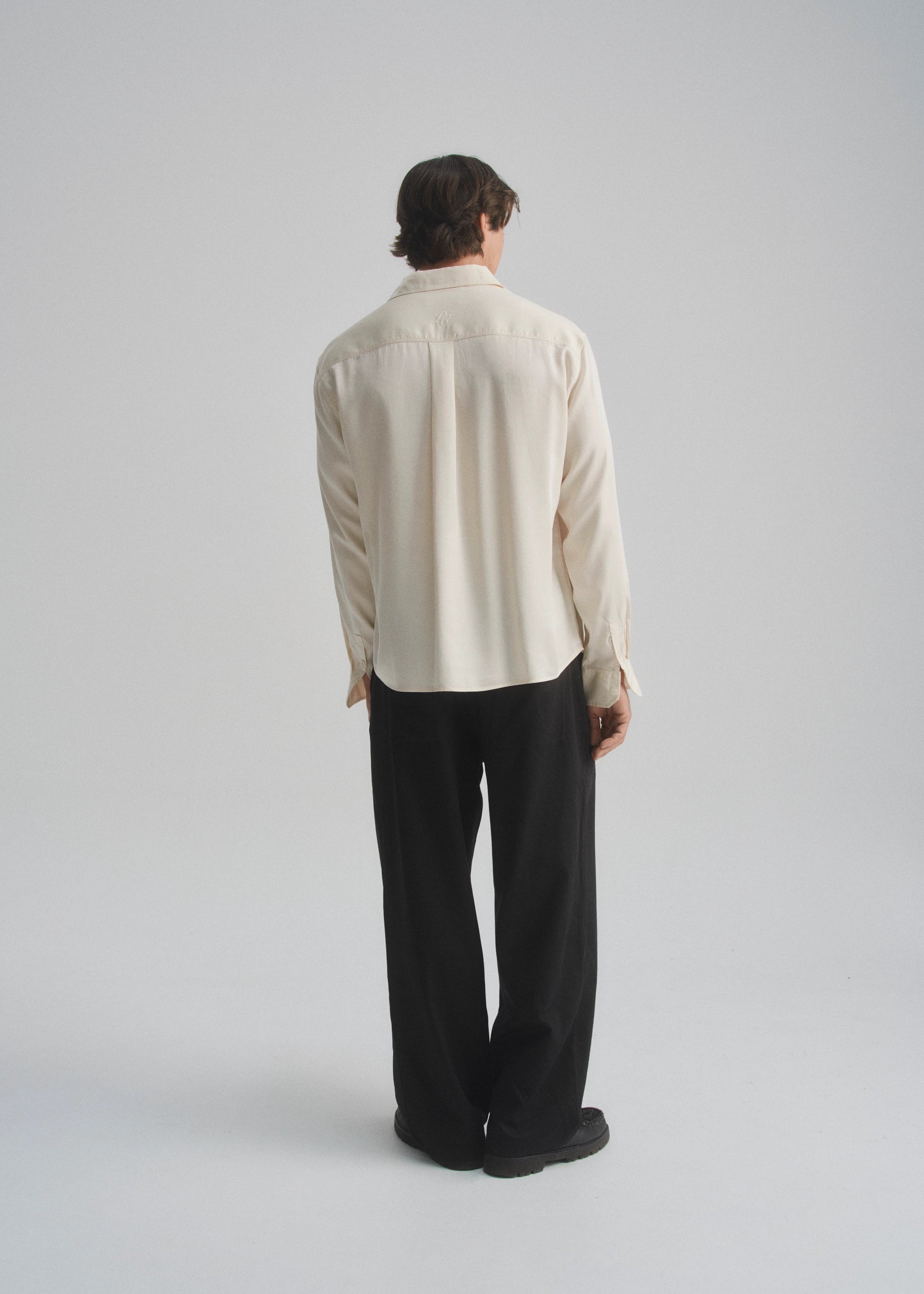 Person wearing a beige shirt and black pants on a plain background