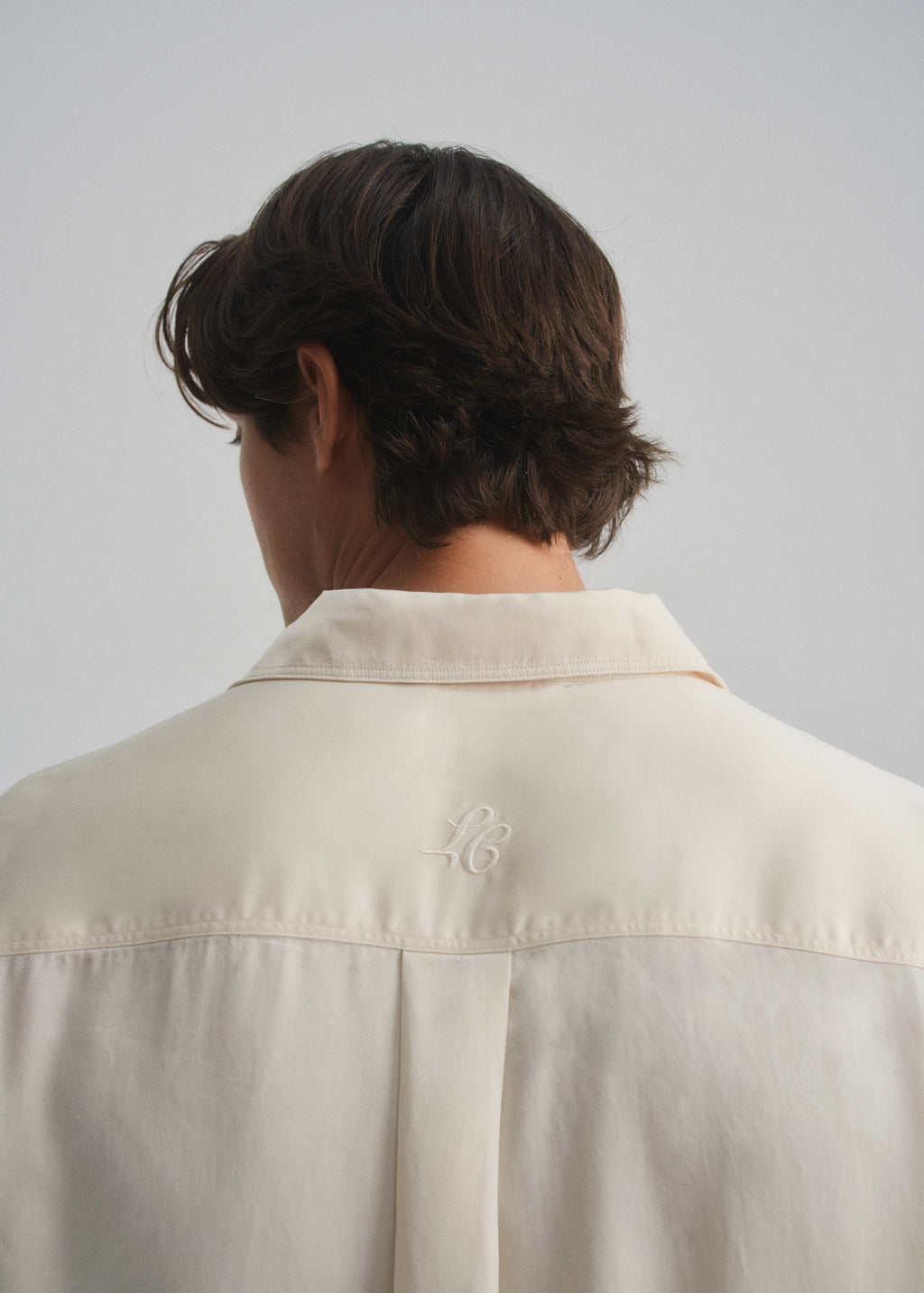 Person wearing a cream shirt with a la corsia brand logo on a plain background