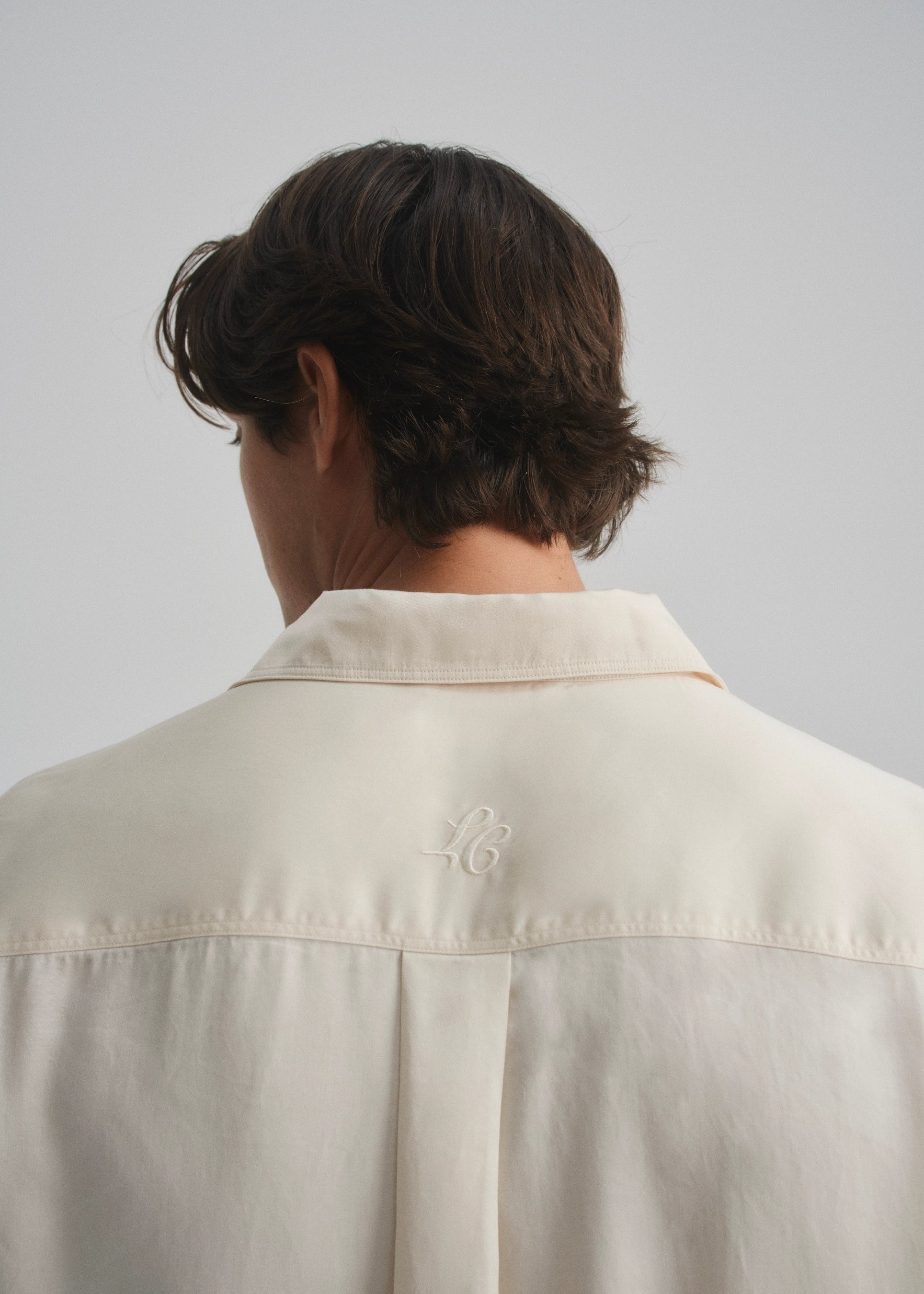 Person wearing a cream shirt with a la corsia brand logo on a plain background