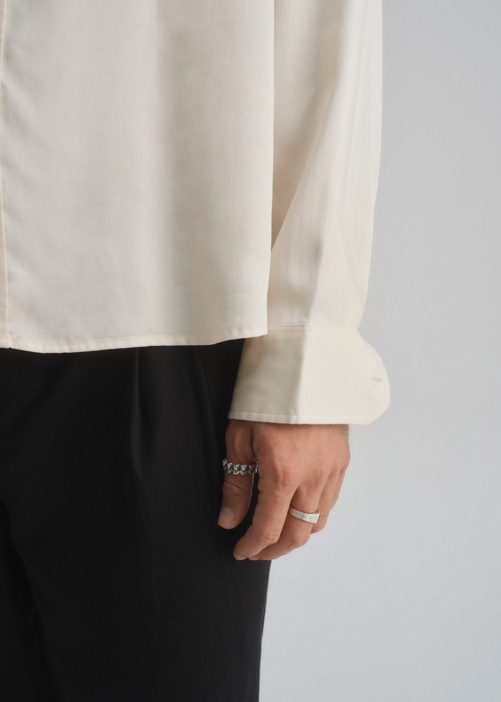 Person wearing a cream ivory shirt and black pants with a plain background