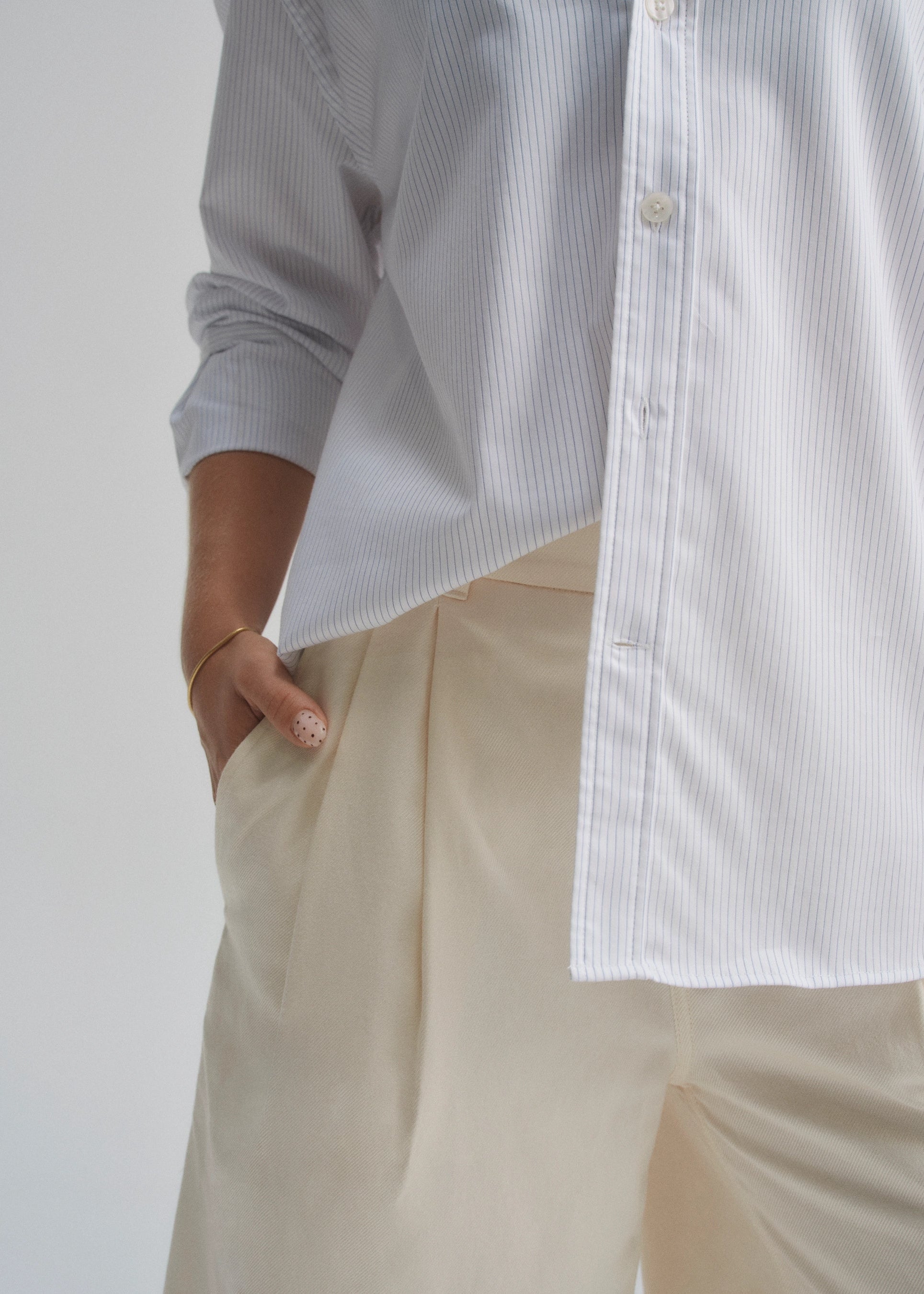 Person wearing a light blue striped shirt and beige pants against a white background