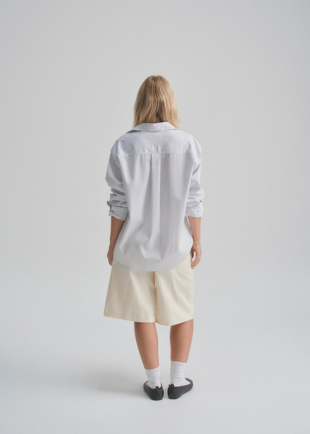 Person wearing a light gray shirt and beige shorts on a plain background