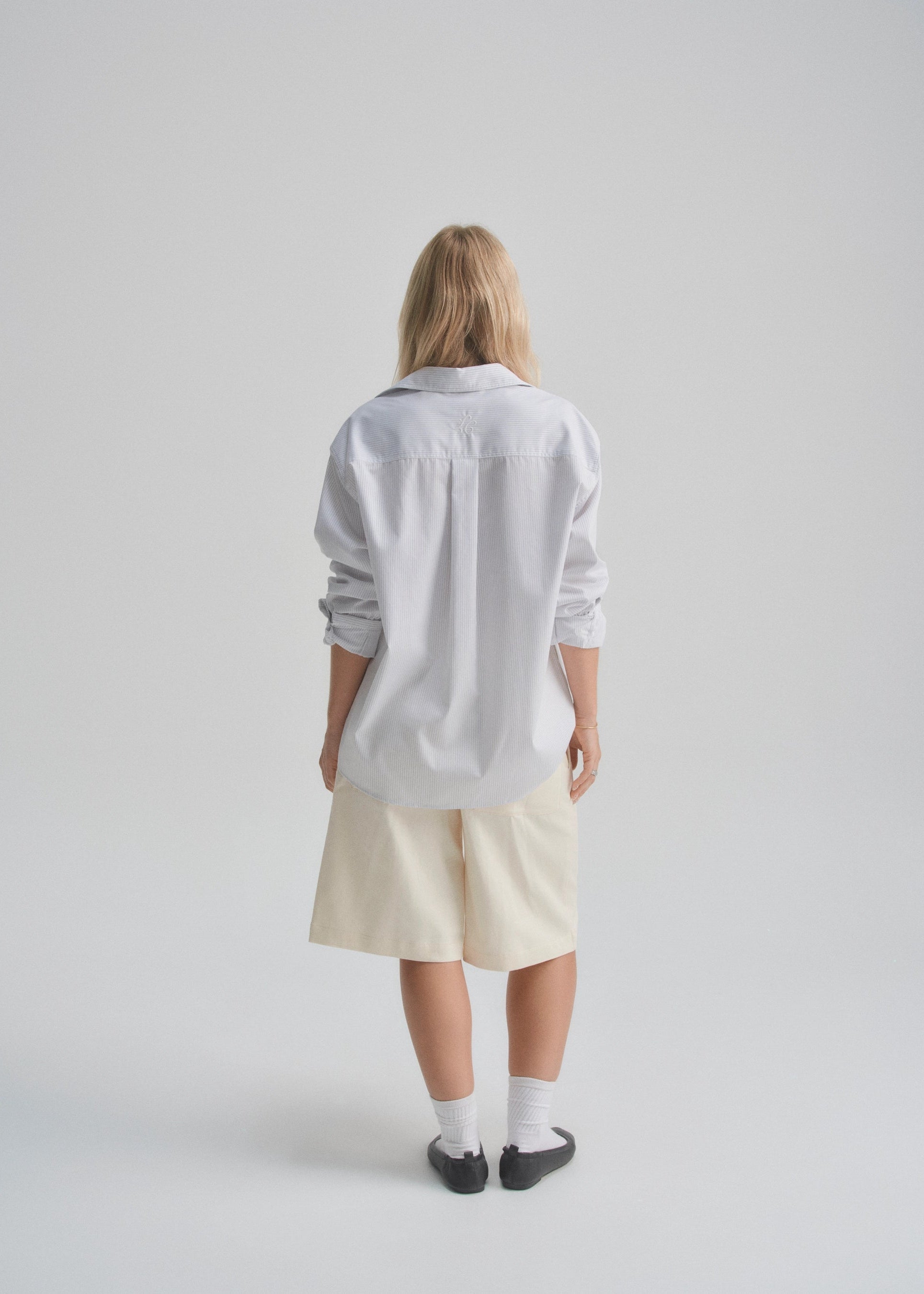 Person wearing a light gray shirt and beige shorts on a plain background