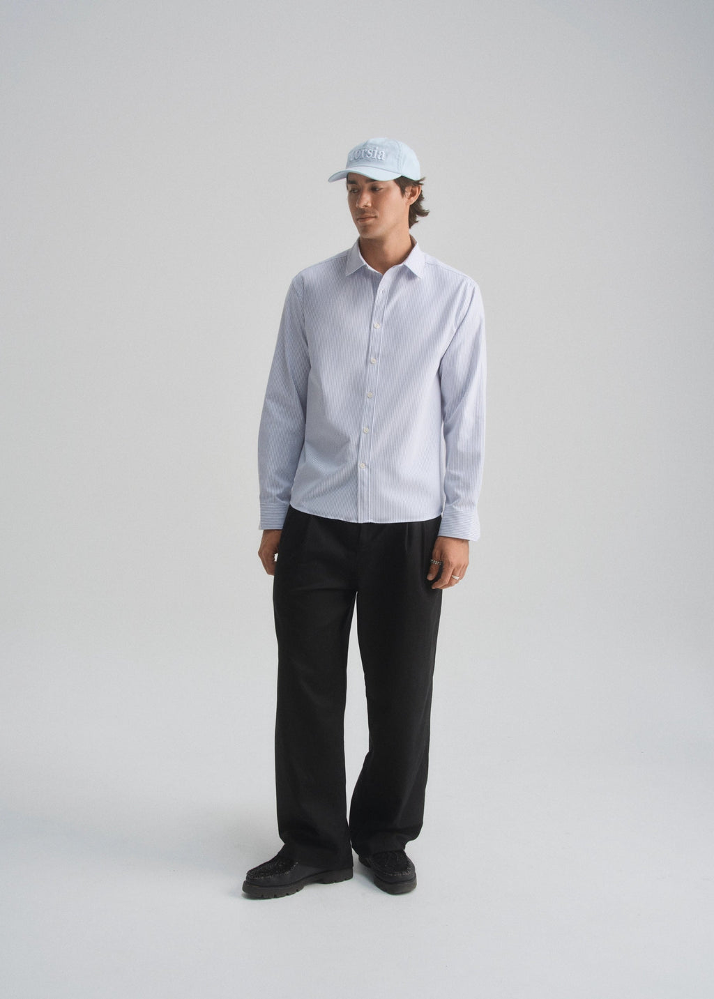 Model wearing a light blue oxford stripe shirt and black pants on a white background