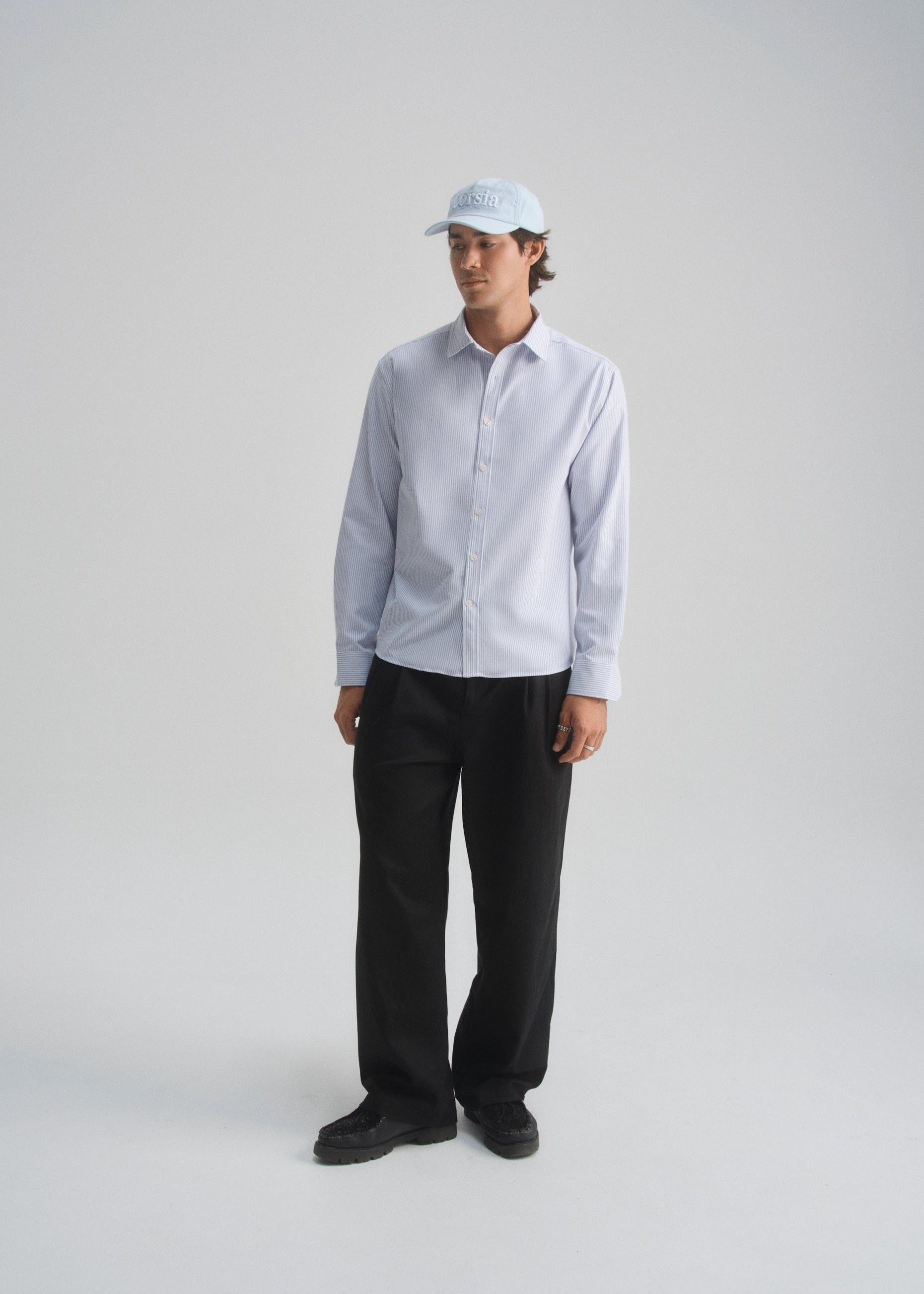 Model wearing a light blue oxford stripe shirt and black pants on a white background