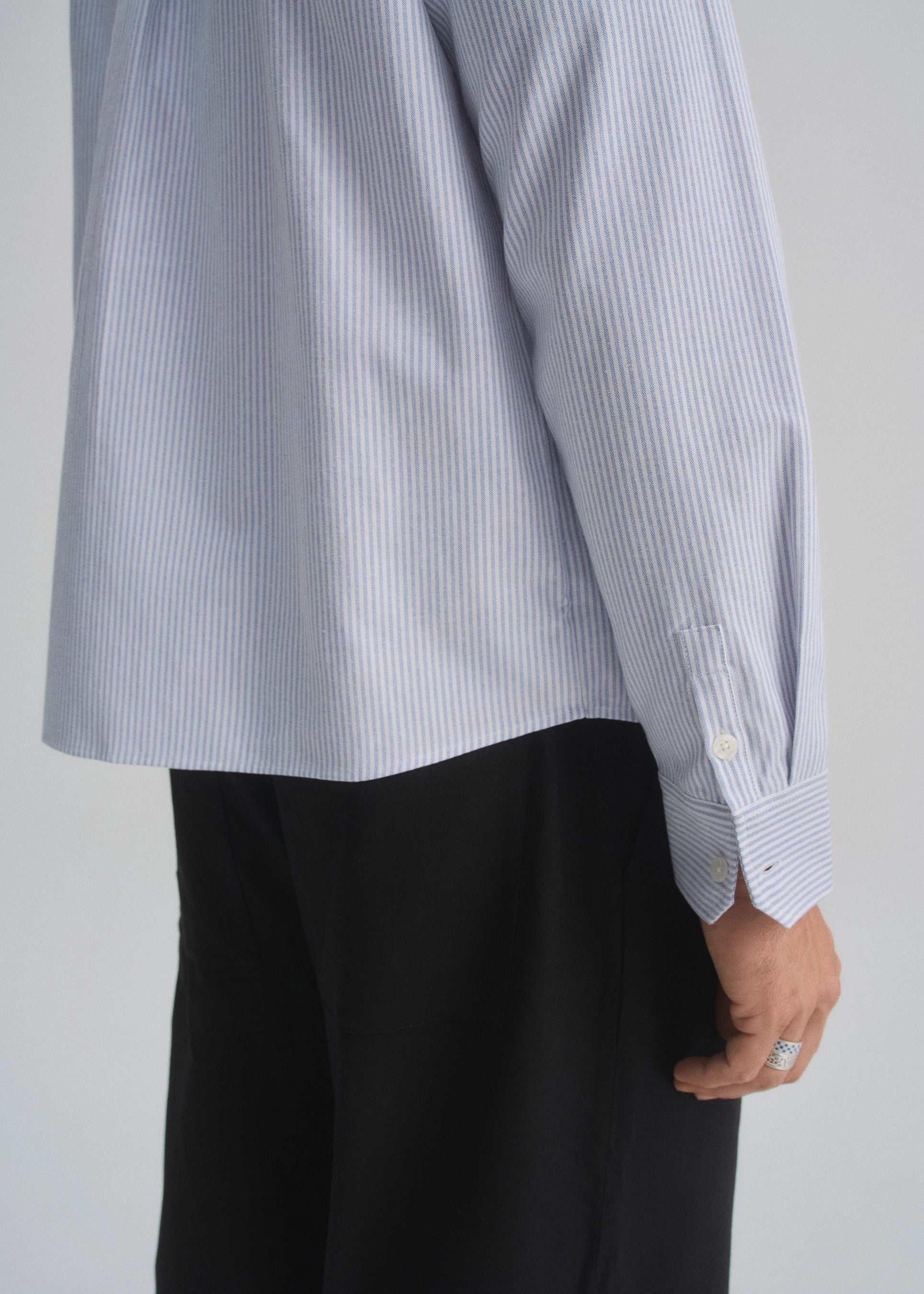 Person wearing a light blue and white striped shirt with black pants on a plain background