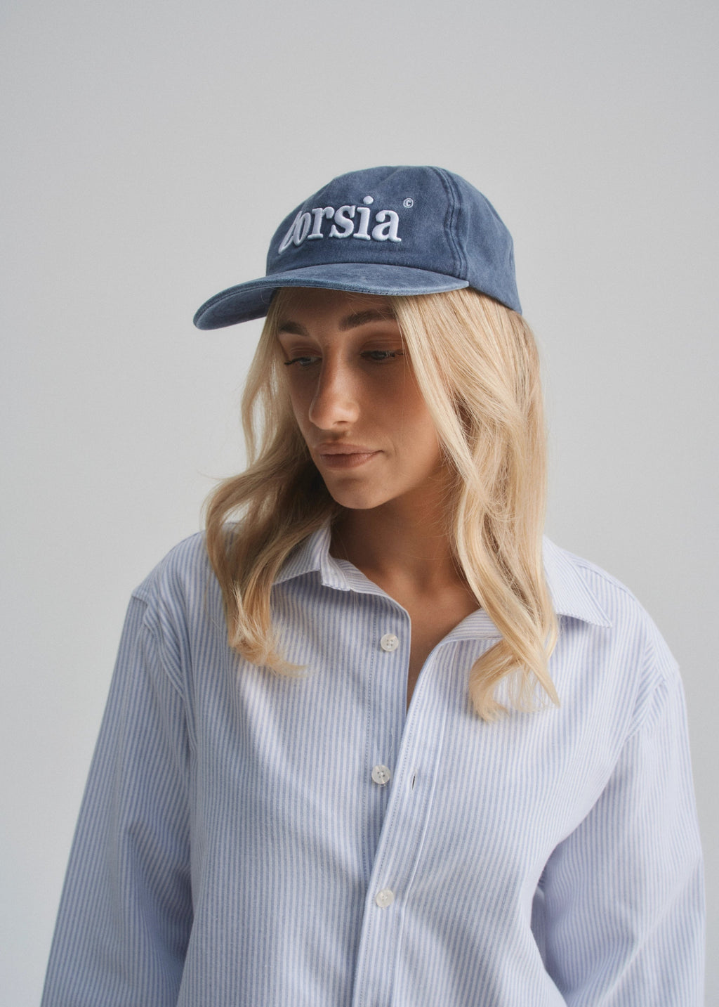 Woman wearing a blue cap with 'Corsia' branding against a plain background