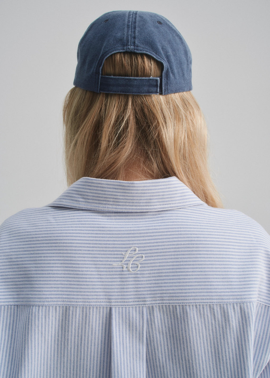Person wearing a faded navy cap and striped shirt with a logo on a plain background