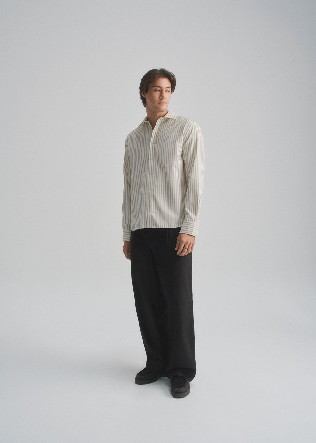 Person wearing a striped cream and brown shirt and black pants on a white background
