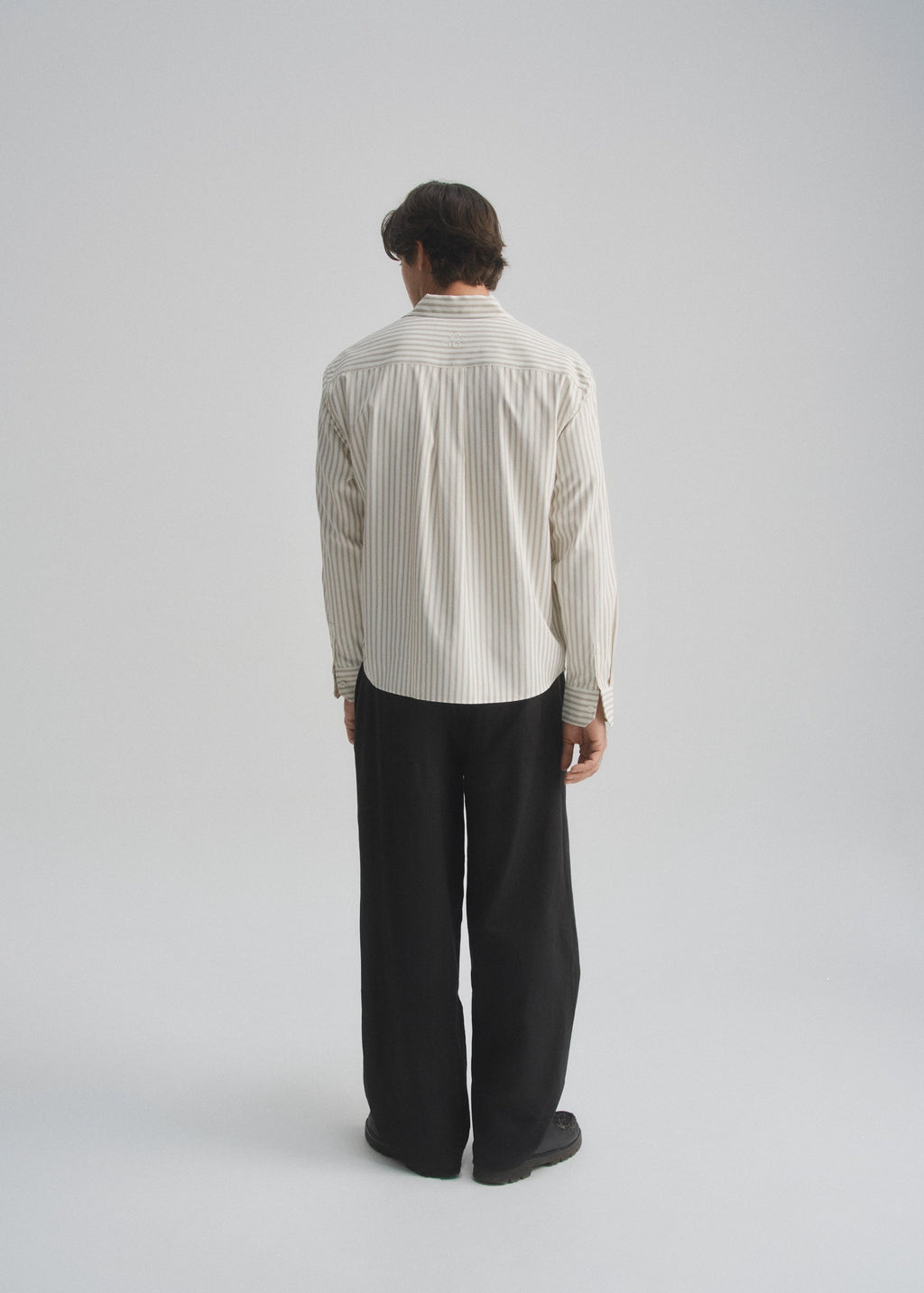 Person wearing a light-cream and brown striped shirt and dark pants on a plain background