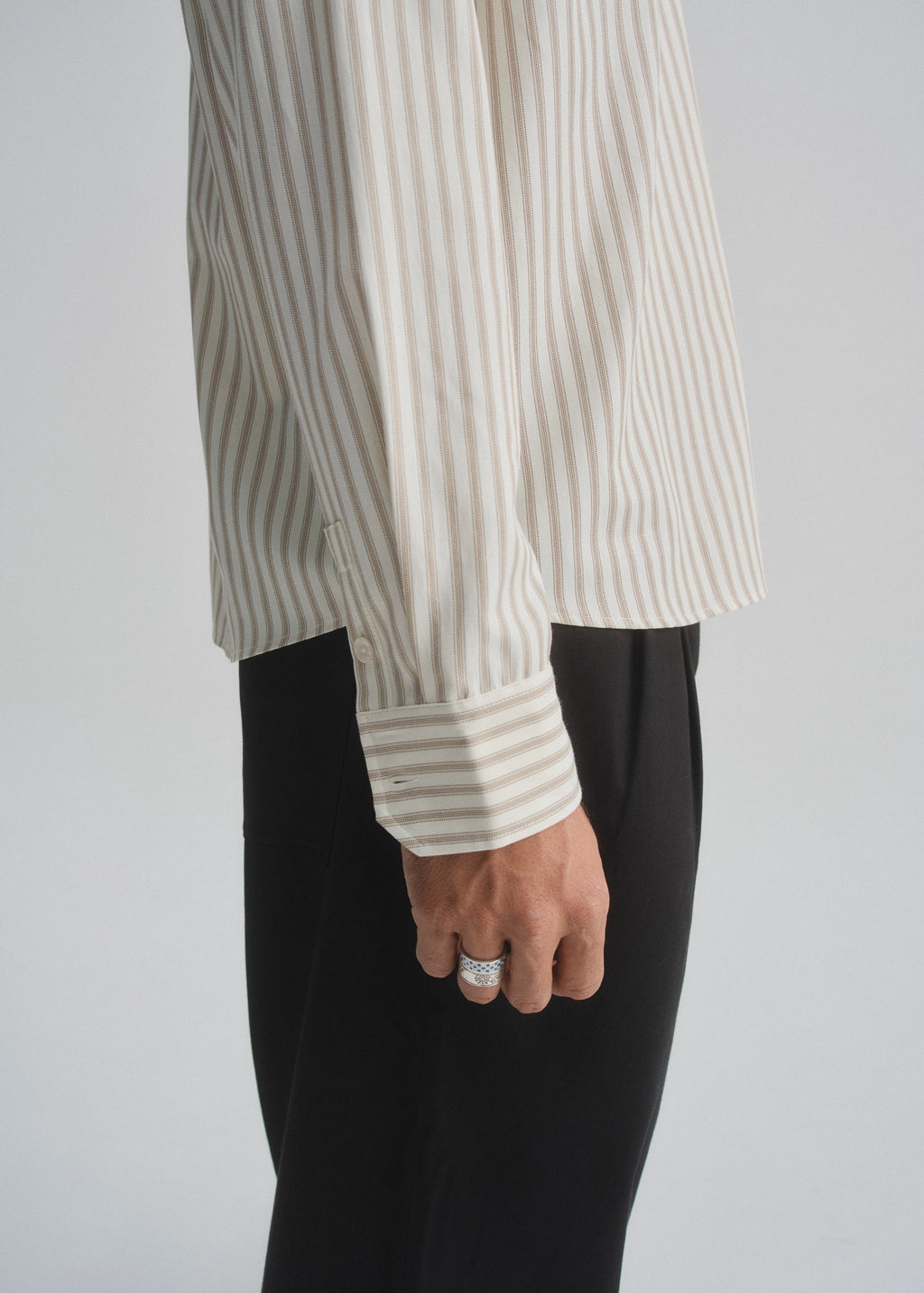 Person wearing a striped cream and brown shirt and black pants on a plain background