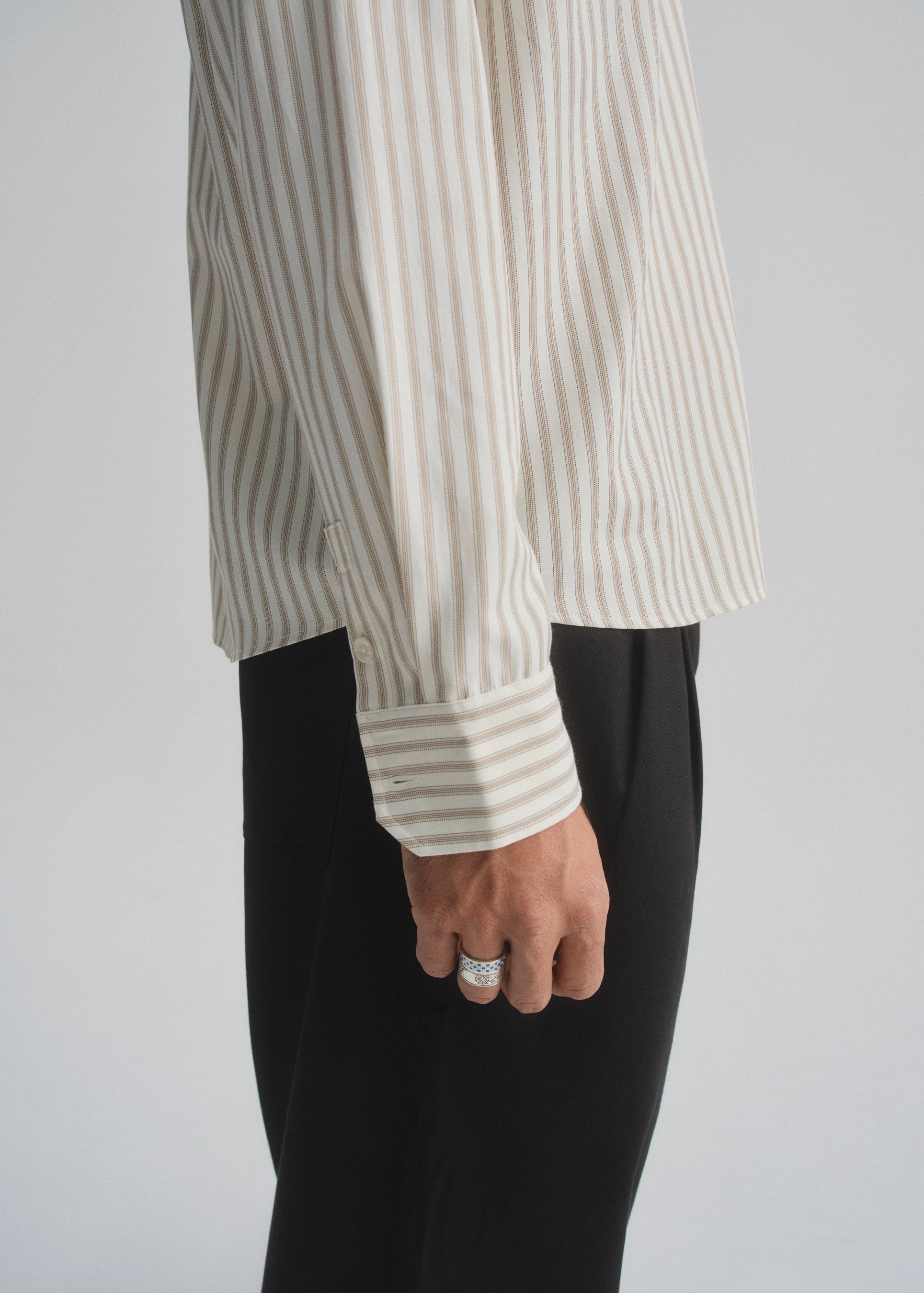 Person wearing a striped cream and brown shirt and black pants on a plain background