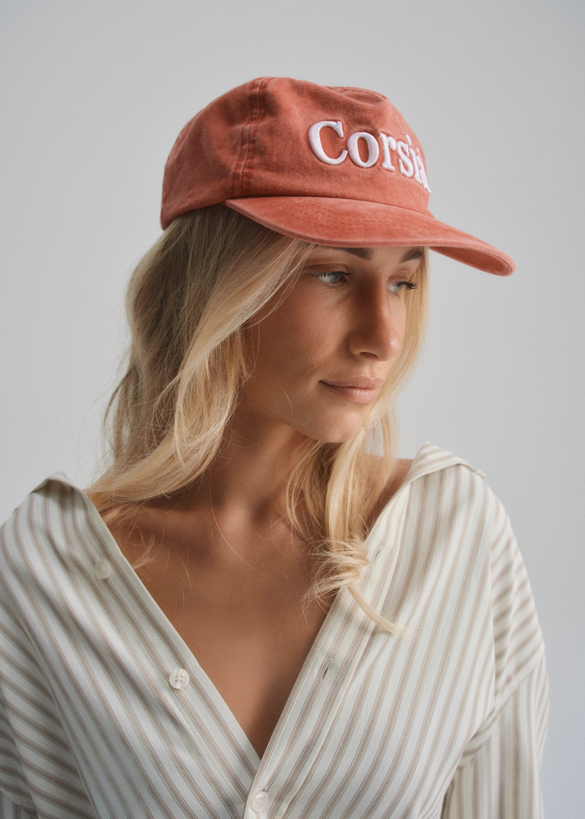 Woman wearing a red cap with 'Corsia' text on a plain background