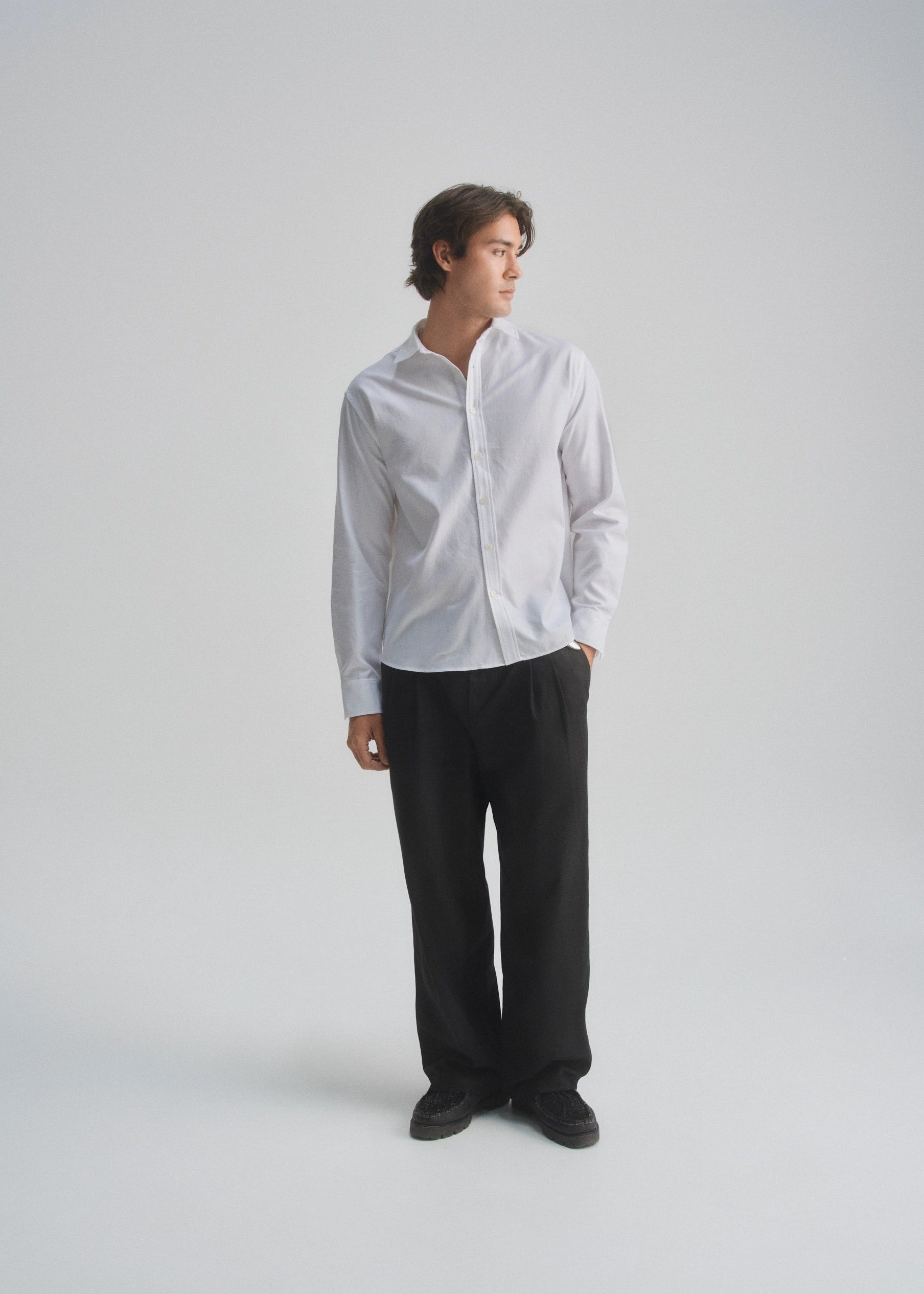 Person wearing a light gray button-up shirt and black pants on a white background