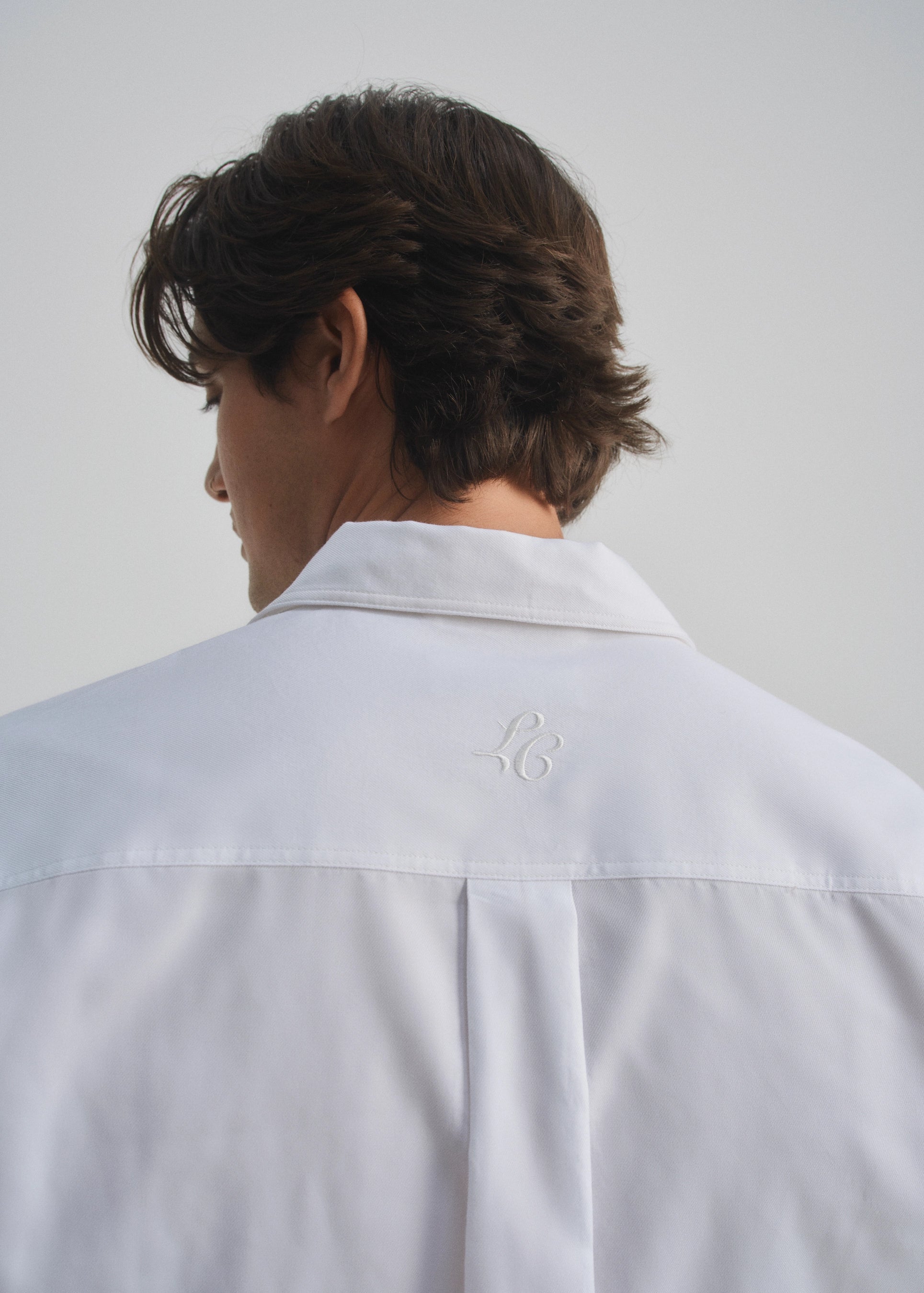 Person wearing a white shirt with a small monogram la corsia logo on a plain background