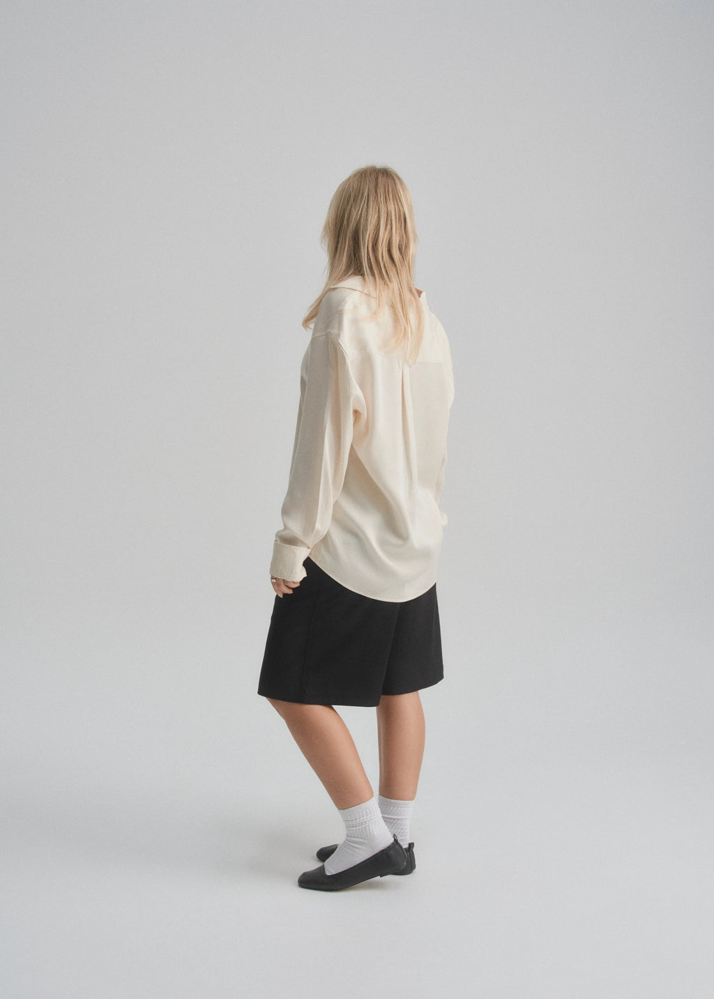 Female model wearing a white sweater and black wide leg shorts on a plain background