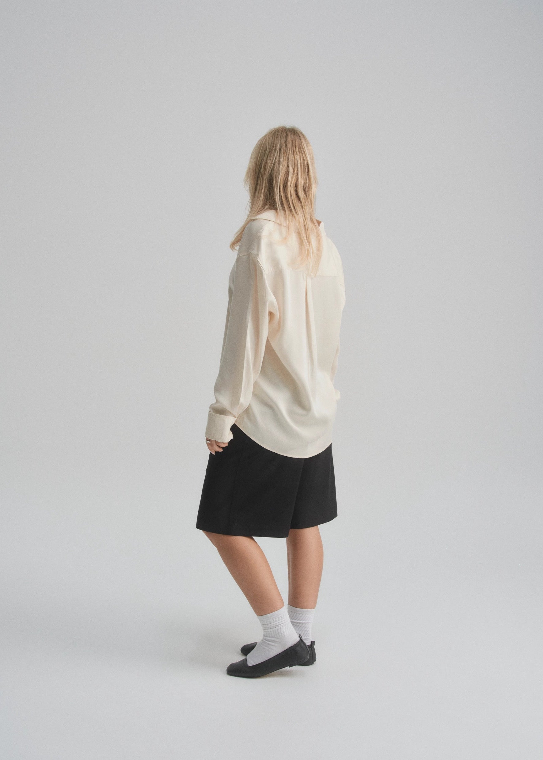 Female model wearing a white sweater and black wide leg shorts on a plain background