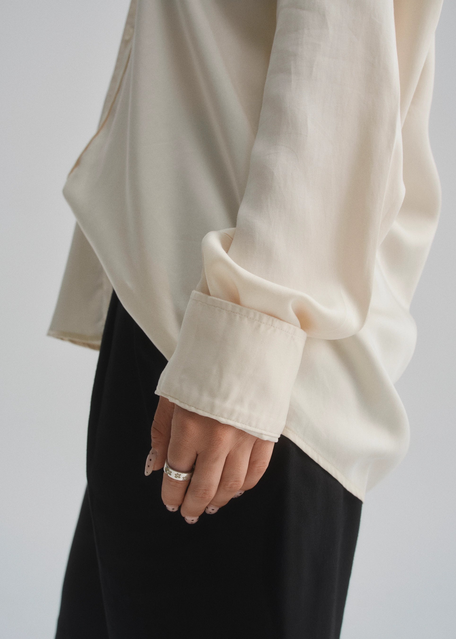 White long-sleeve shirt with rolled-up cuffs and a ring on a plain background