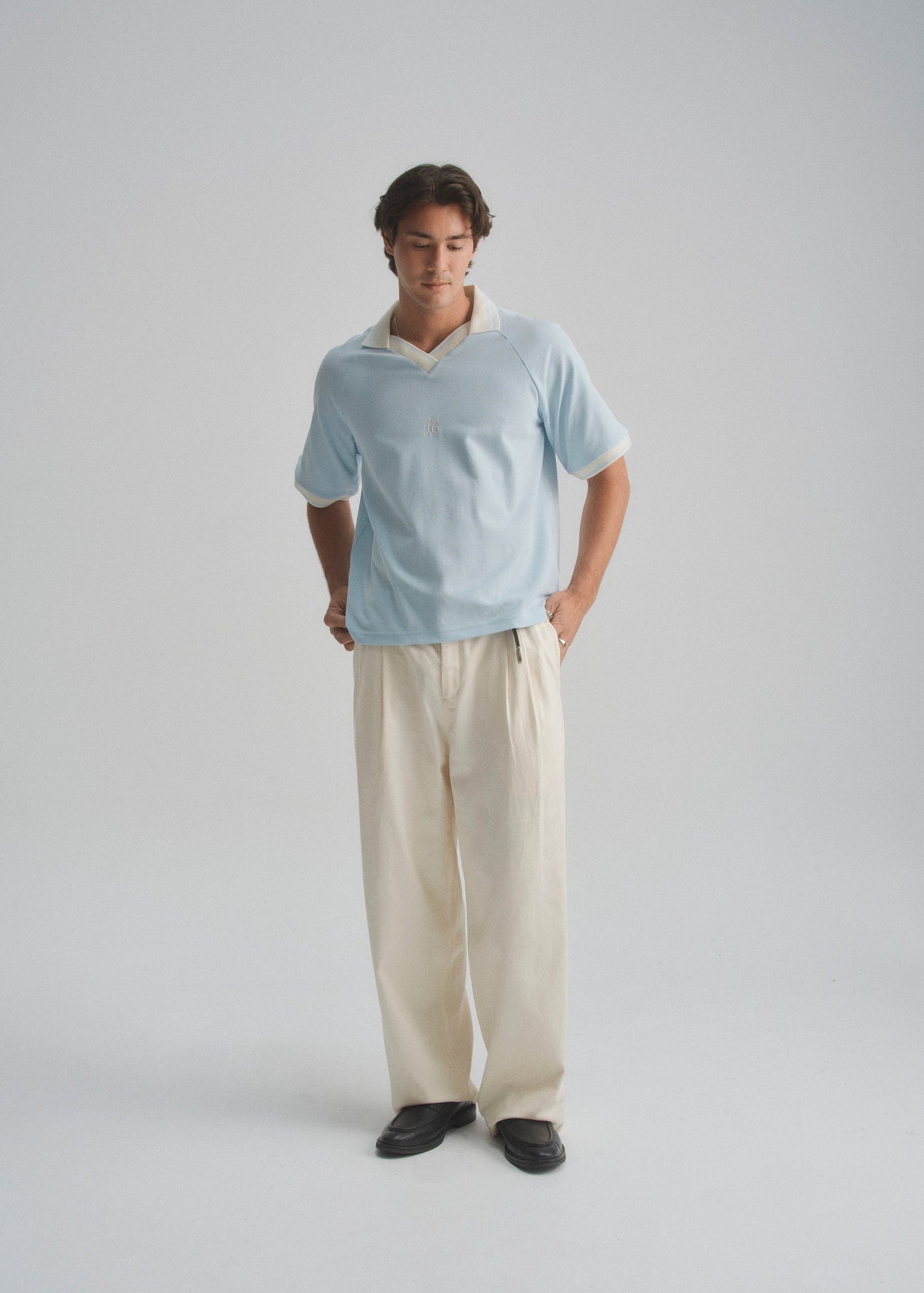 Man wearing a light blue shirt and beige pants on a plain background