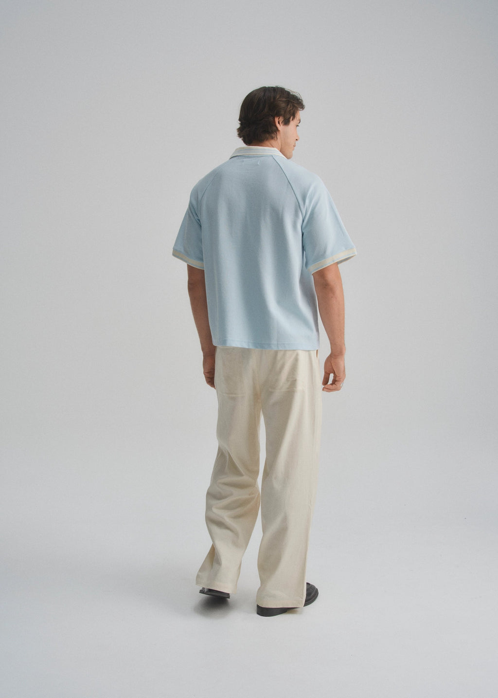 Person wearing a light blue shirt and beige pants on a plain background