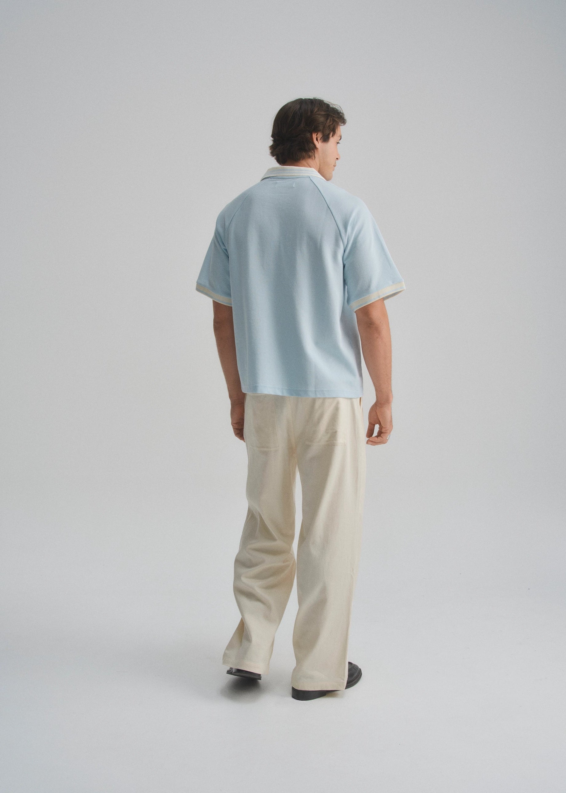 Person wearing a light blue shirt and beige pants on a plain background