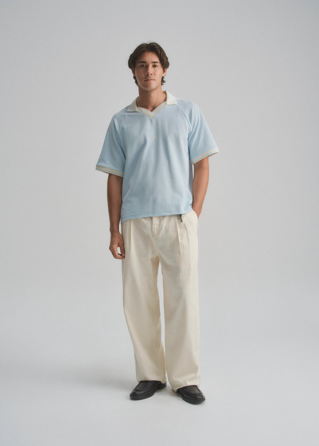 Man wearing a light blue pique polo and beige pants on a gray background