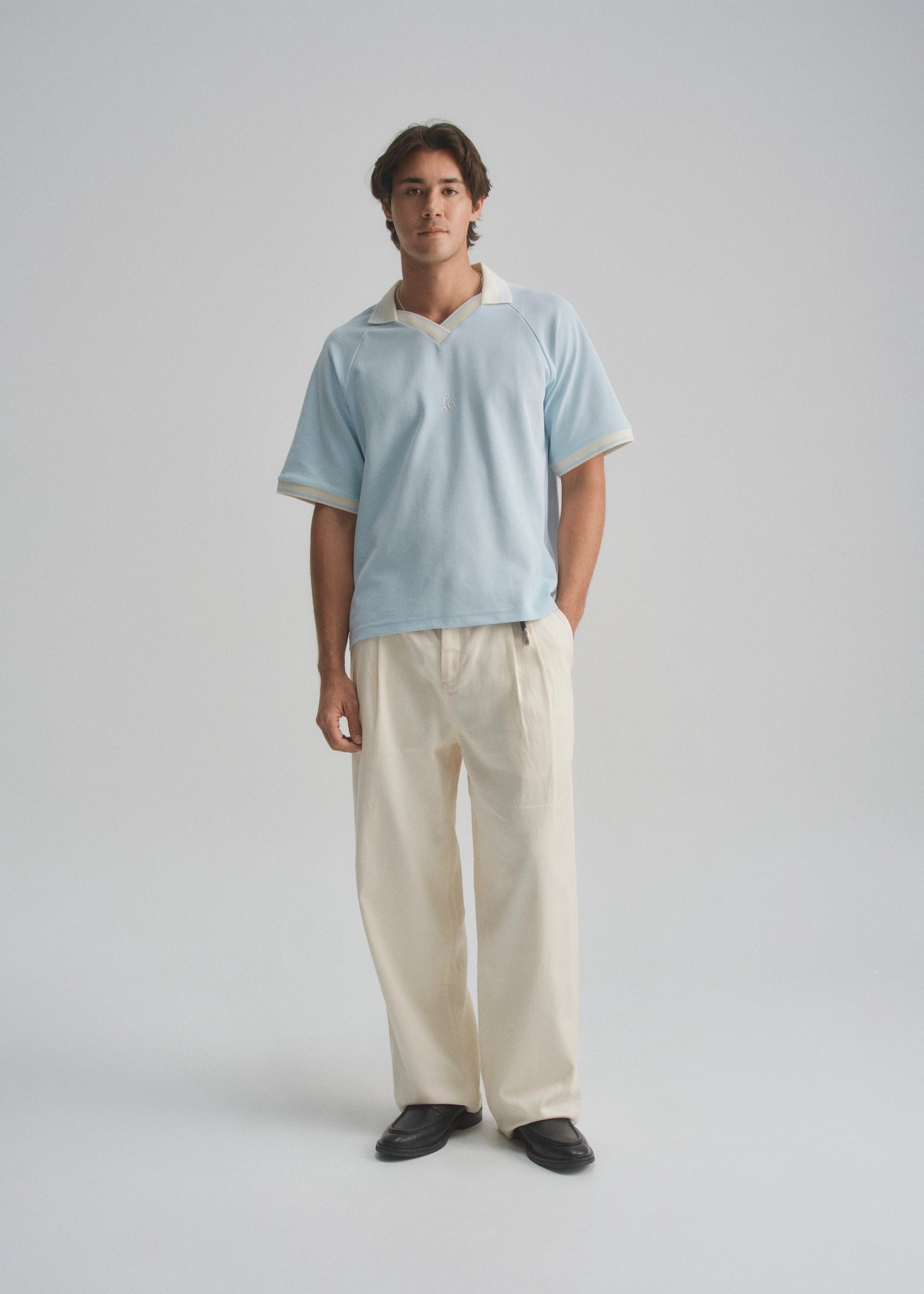 Man wearing a light blue pique polo and beige pants on a gray background