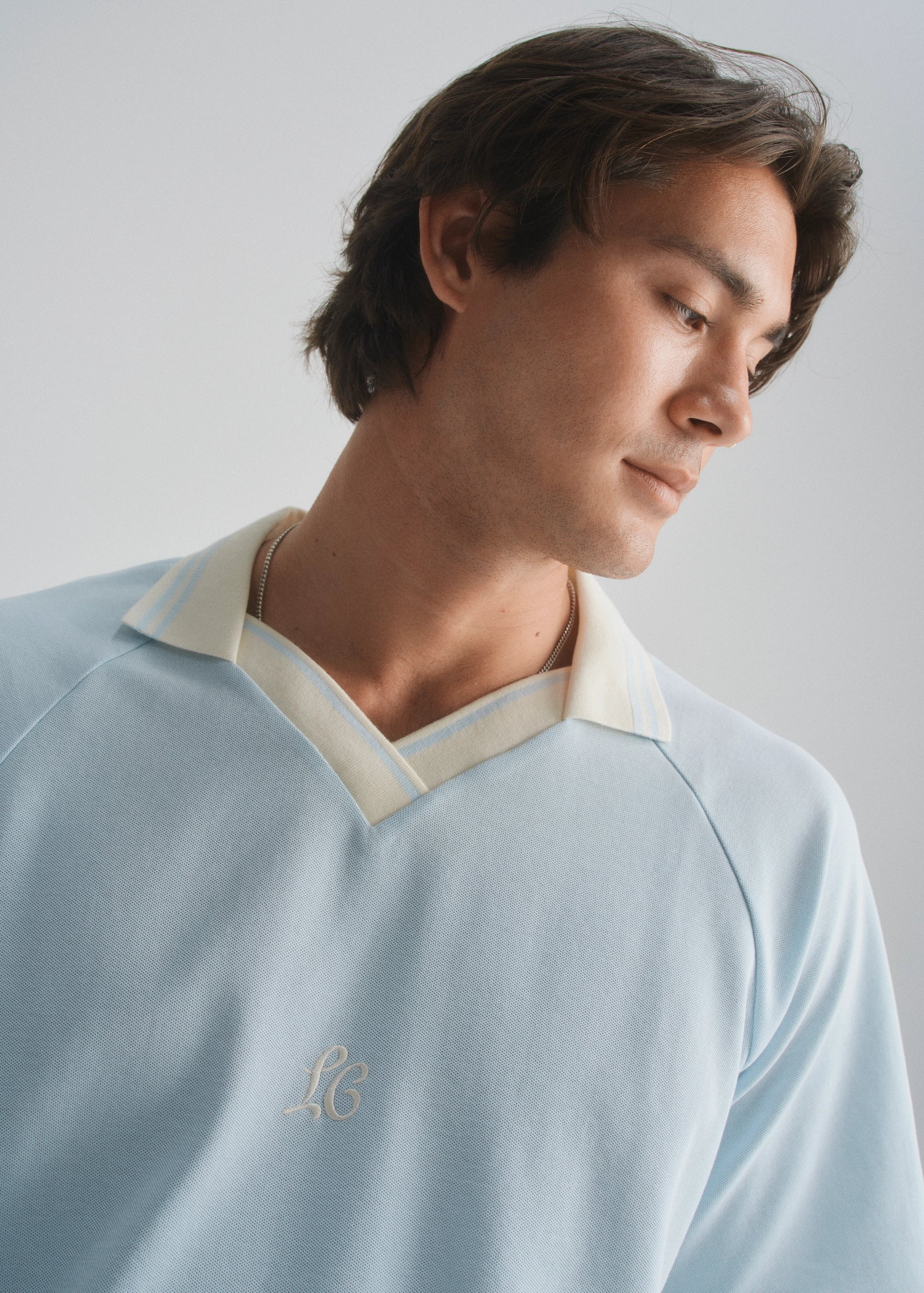 Man wearing a light blue shirt with a logo on a plain background