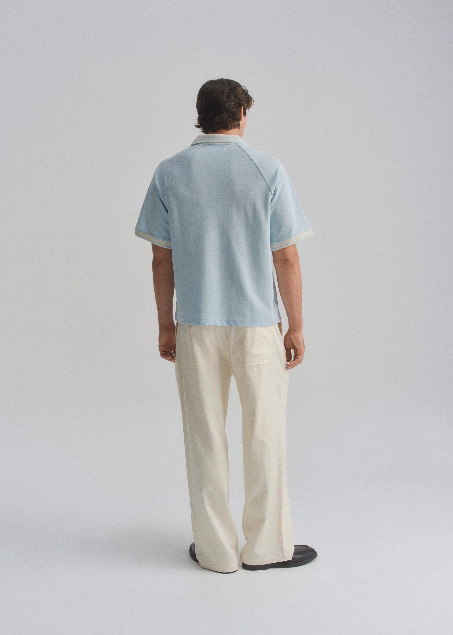 Person wearing a light blue shirt and beige pants on a plain background