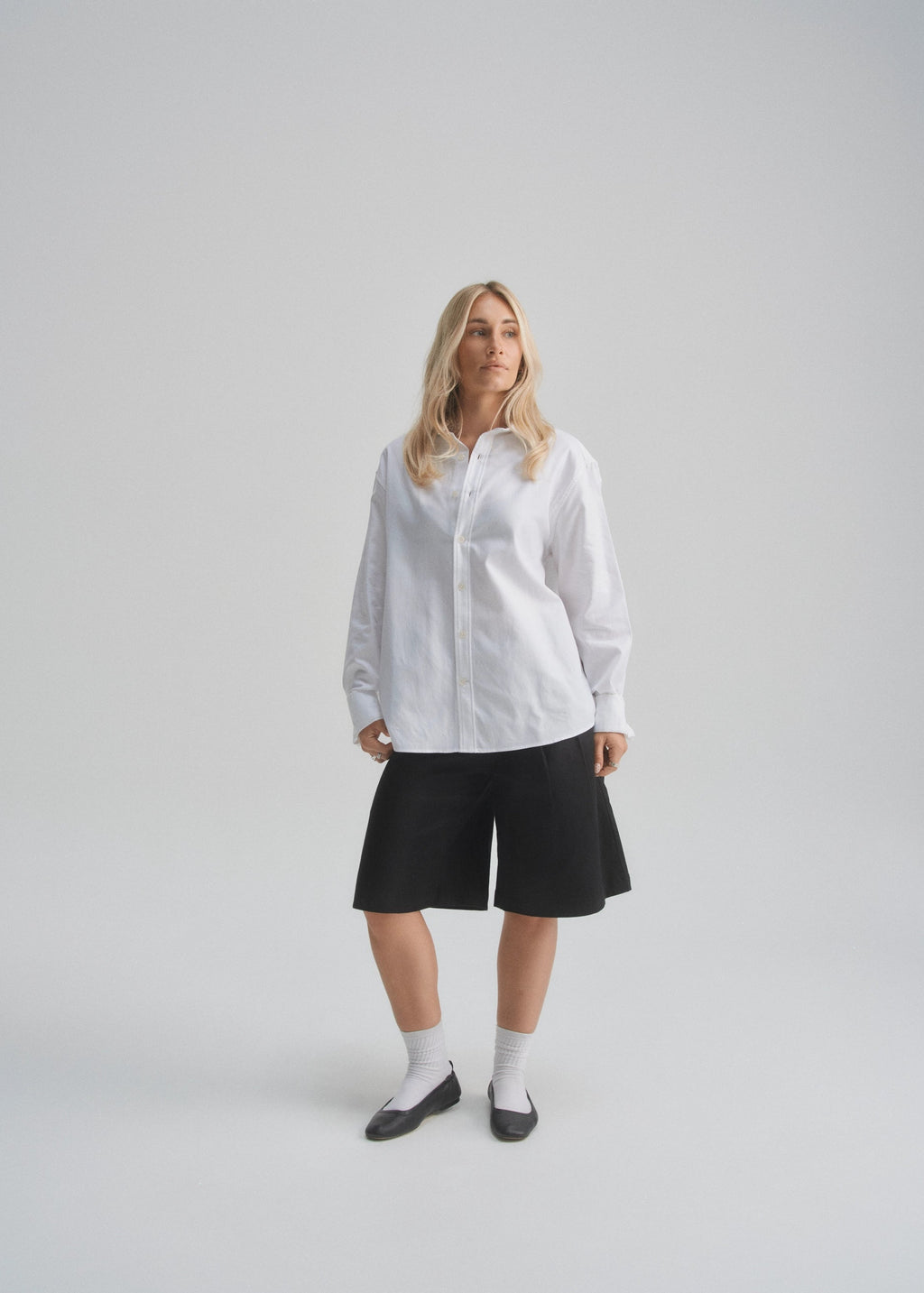 Woman wearing a white shirt and black shorts on a light gray background