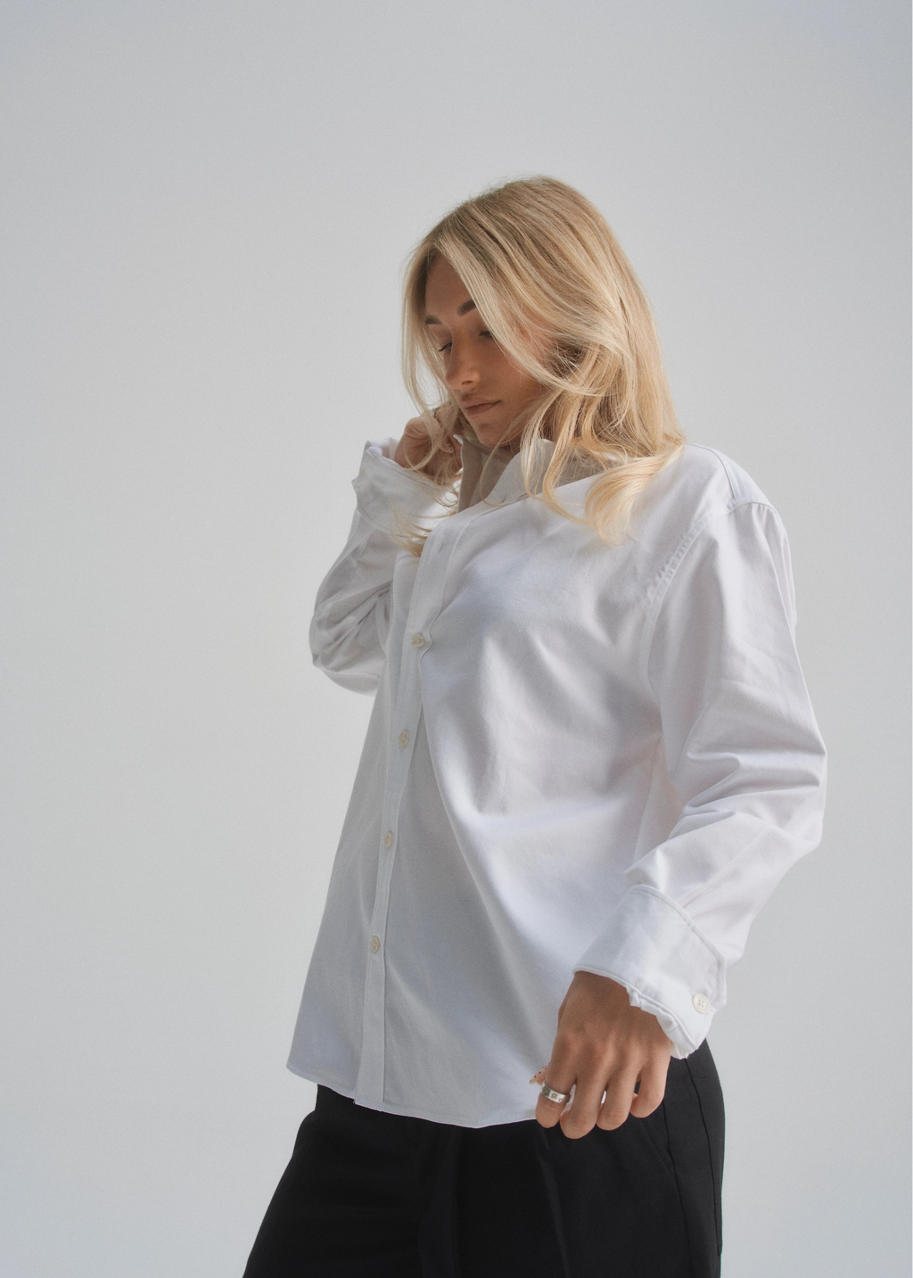 Woman wearing a white button up with long sleeves against a plain background