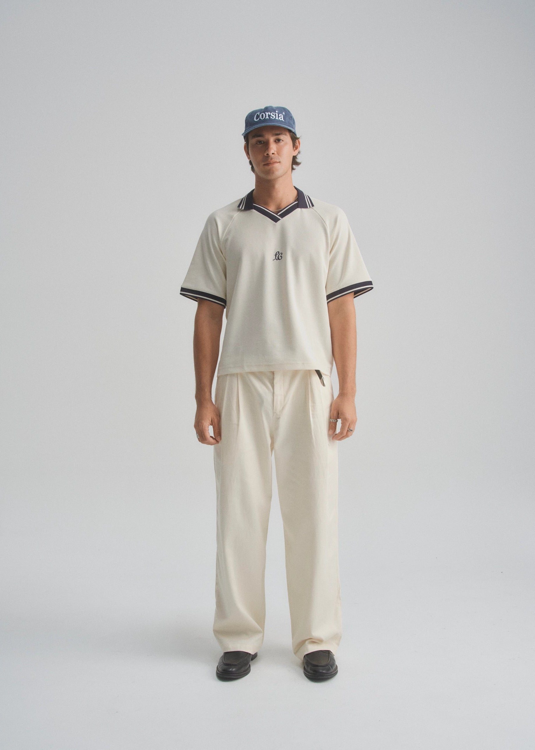 Person wearing a cream pique polo shirt and cream pants with a cap on a gray background