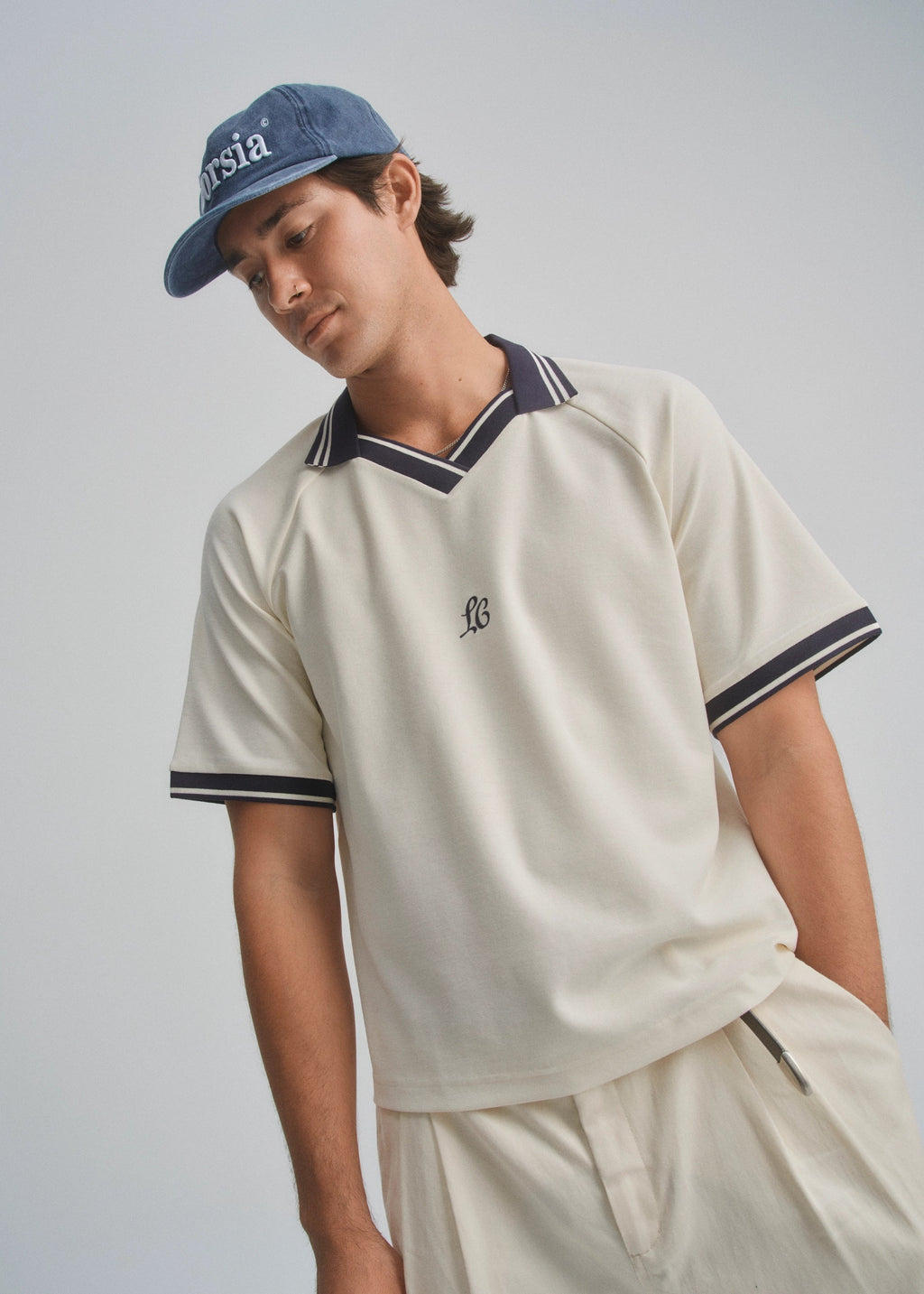 Person wearing a beige polo shirt and cap with a logo on a plain background