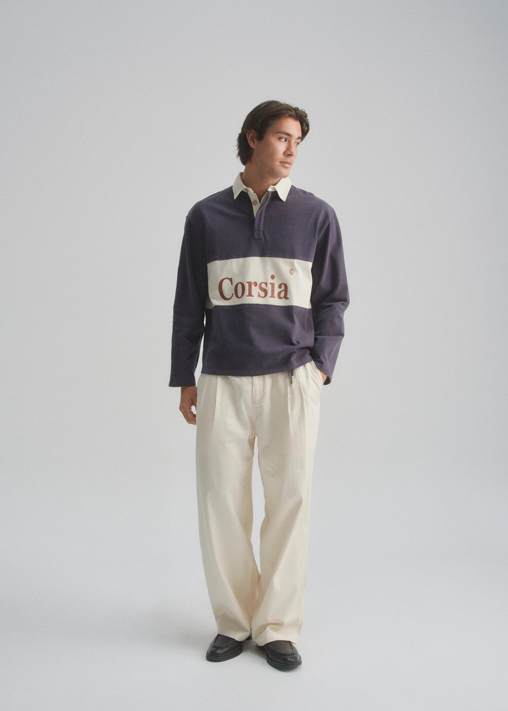 Man wearing a dark purple rugby shirt with 'Corsia' logo on a light gray background