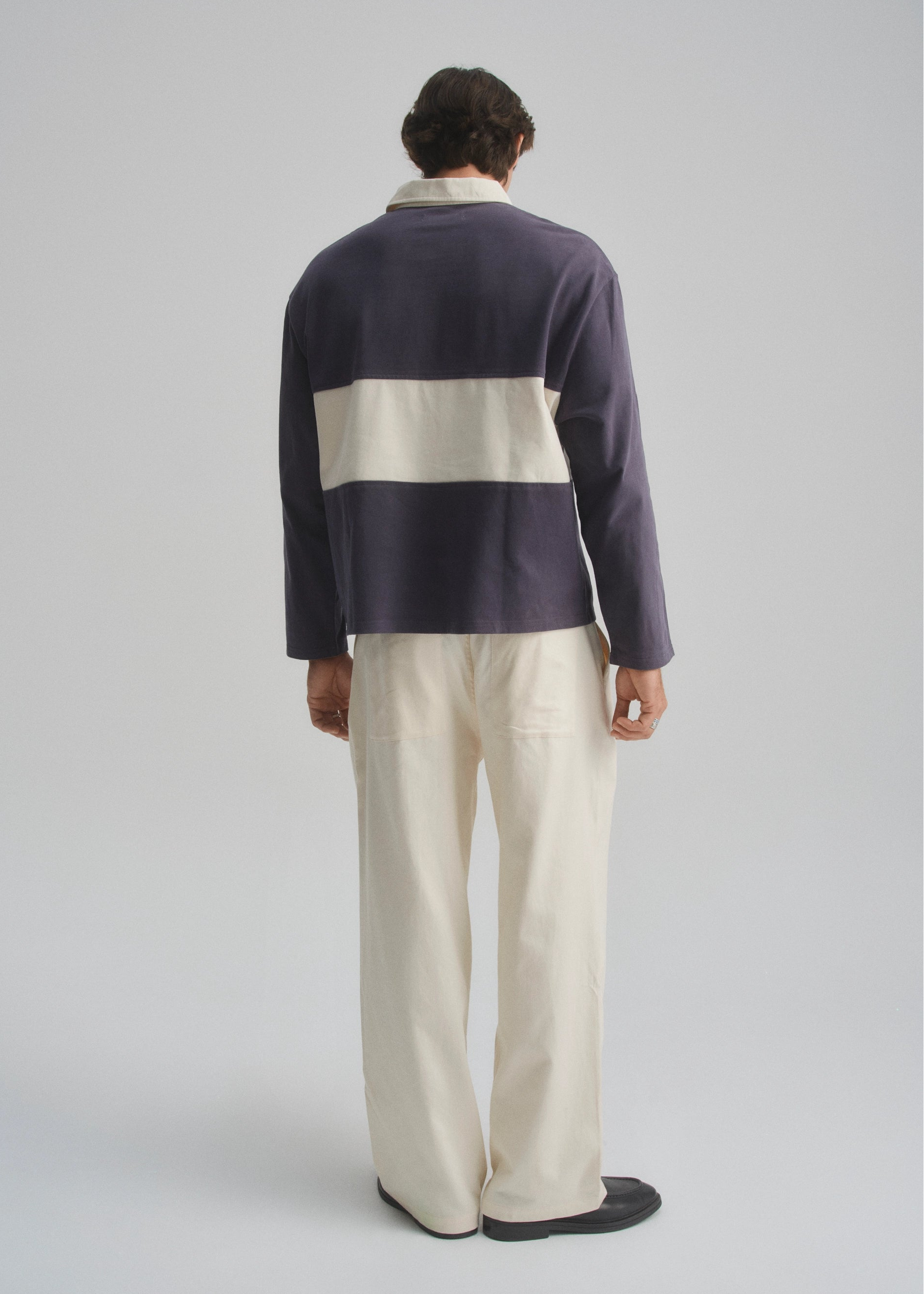 Person wearing a colour block rugby jersey sweater and cream pants on a plain background