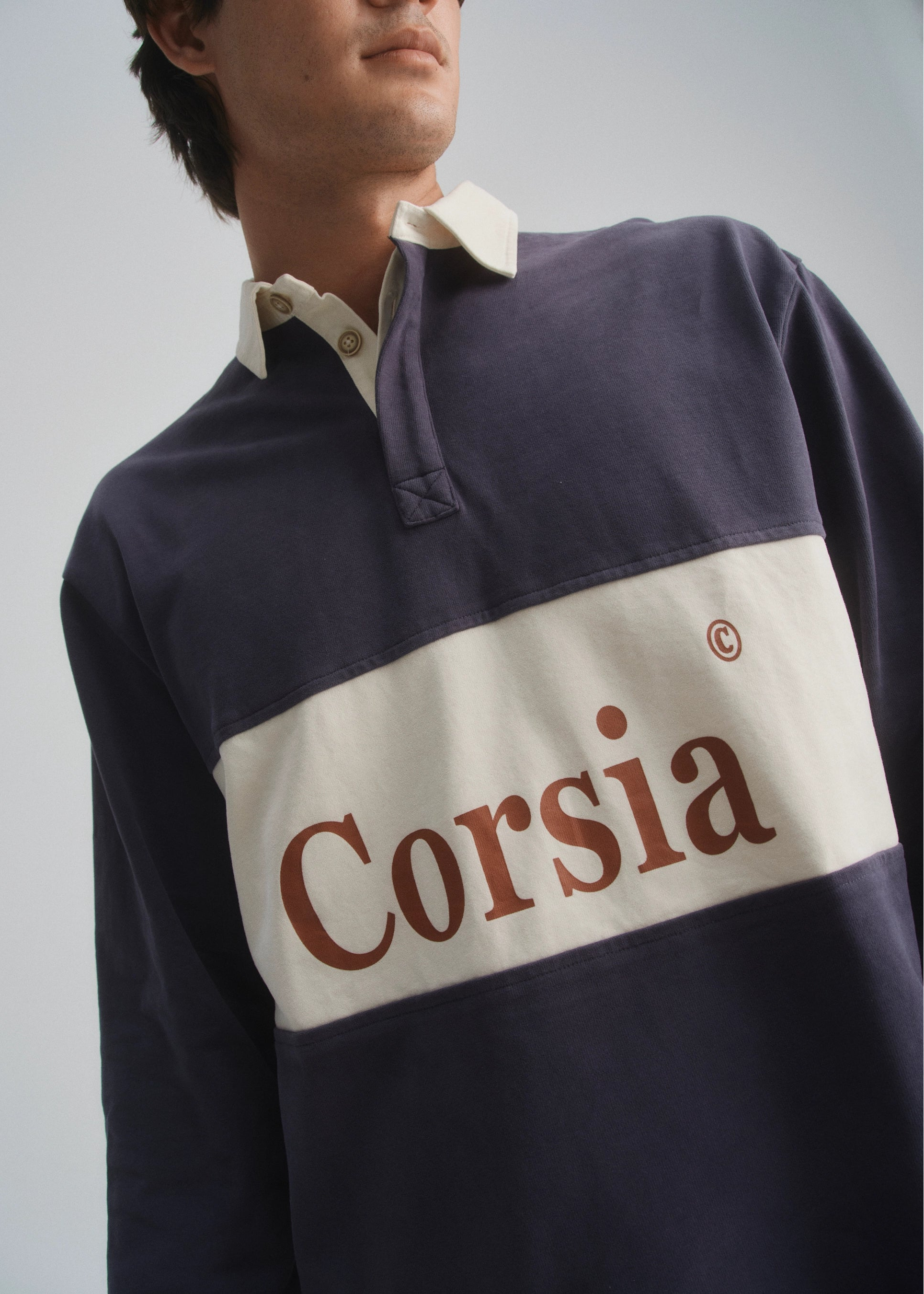 Person wearing a navy and beige rugby-style shirt with 'Corsia' branding.
