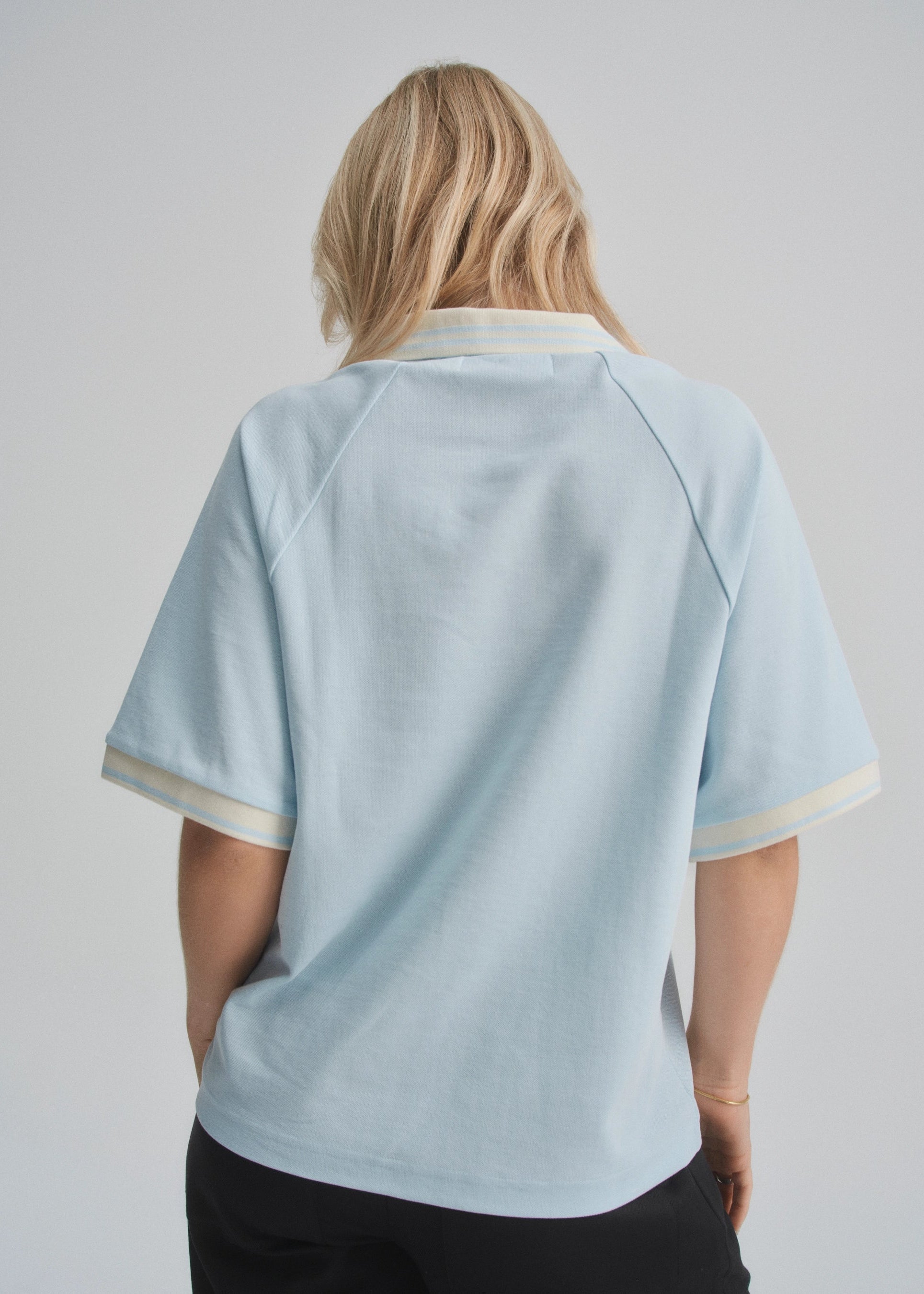 Person wearing a light blue polo shirt with white trim on a plain background