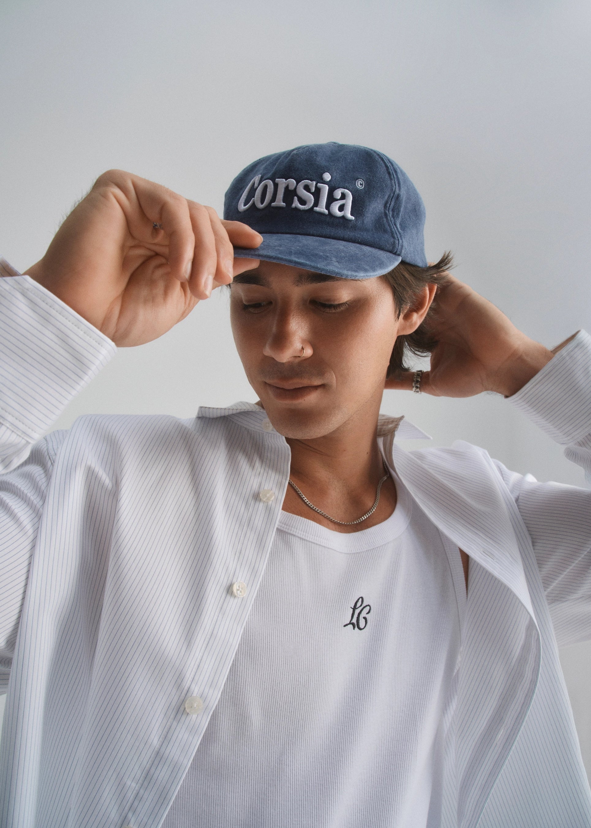 Person wearing a faded navy cap with 'corsia' branding and a white shirt with a La Corsia monogram.