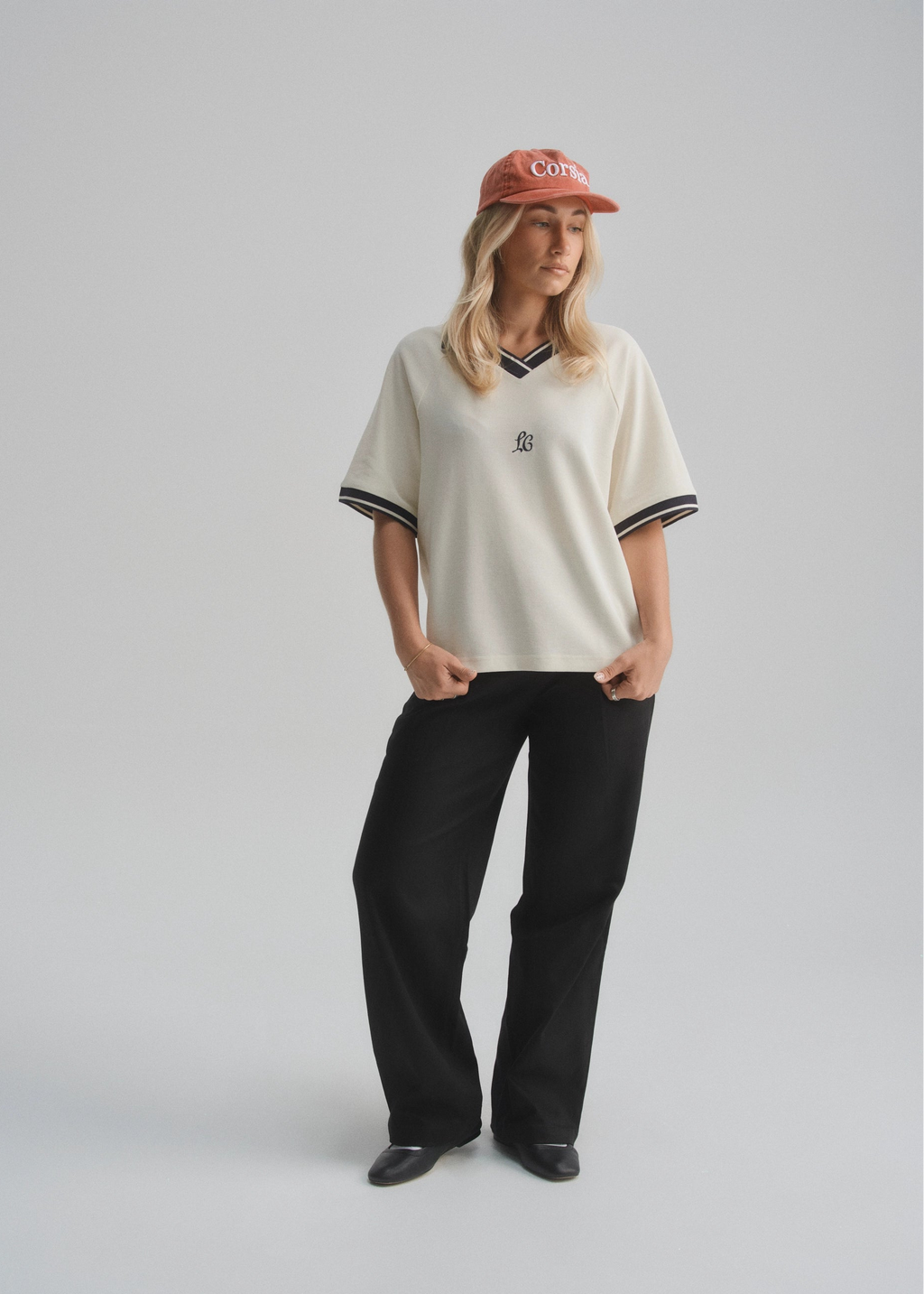 Person wearing a cream pique polo with navy trim and black pants on a gray background