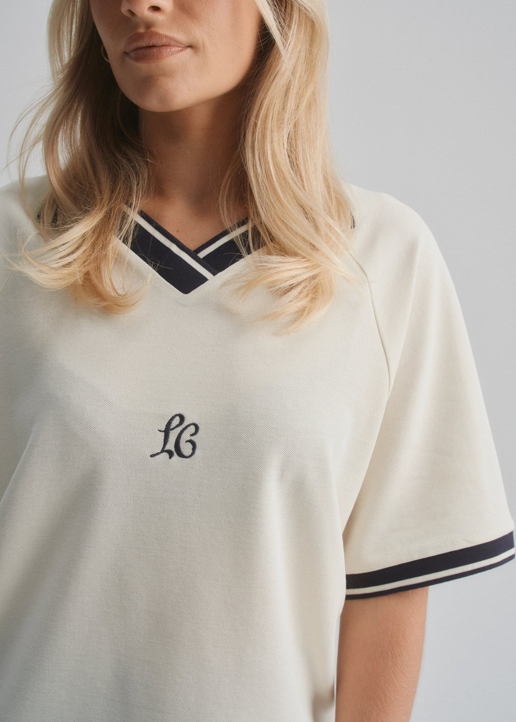 Person wearing a cream pique polo shirt with a logo on a gray background