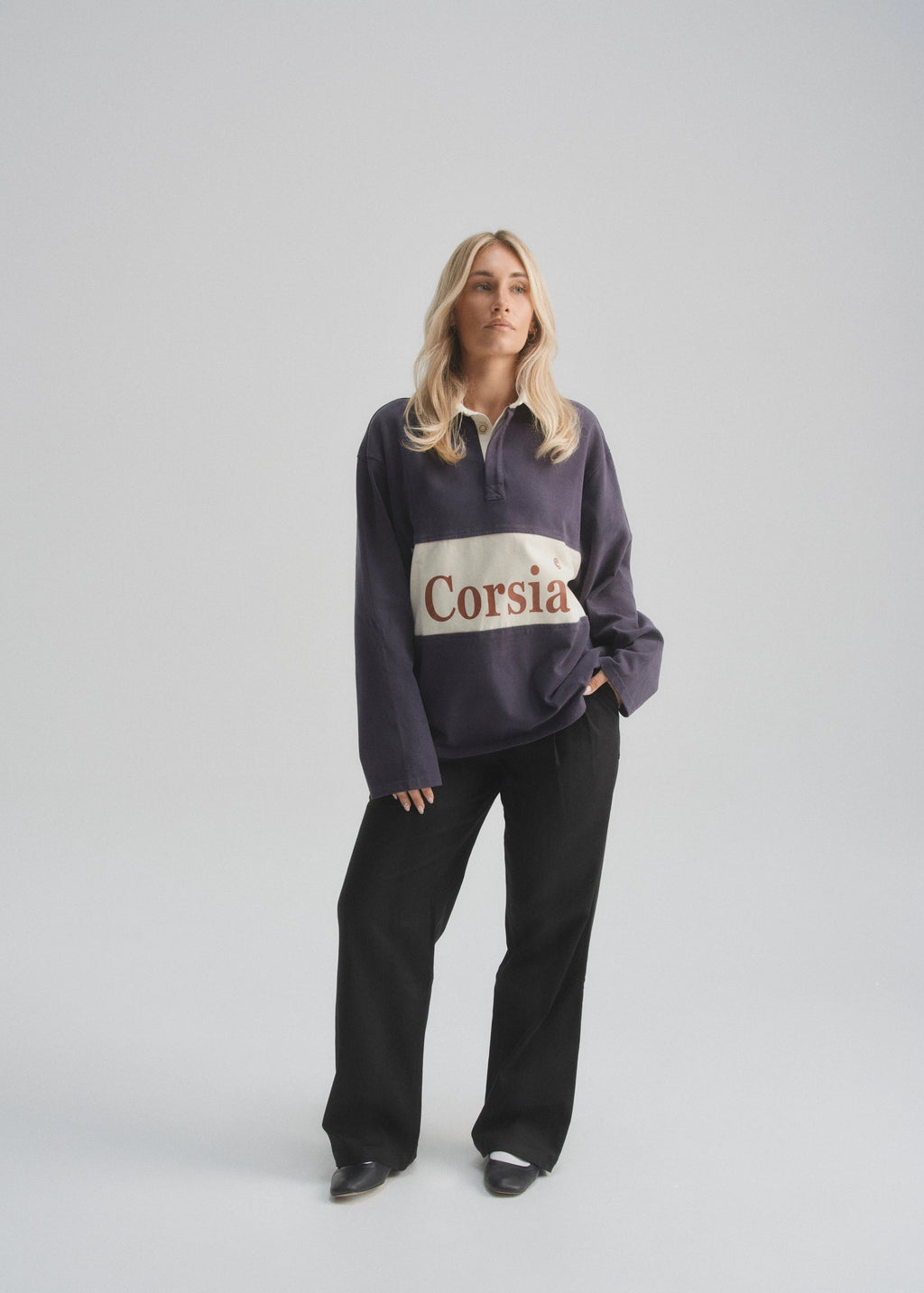 Person wearing a dark faded navy sweatshirt with 'Corsia' logo on a light gray background