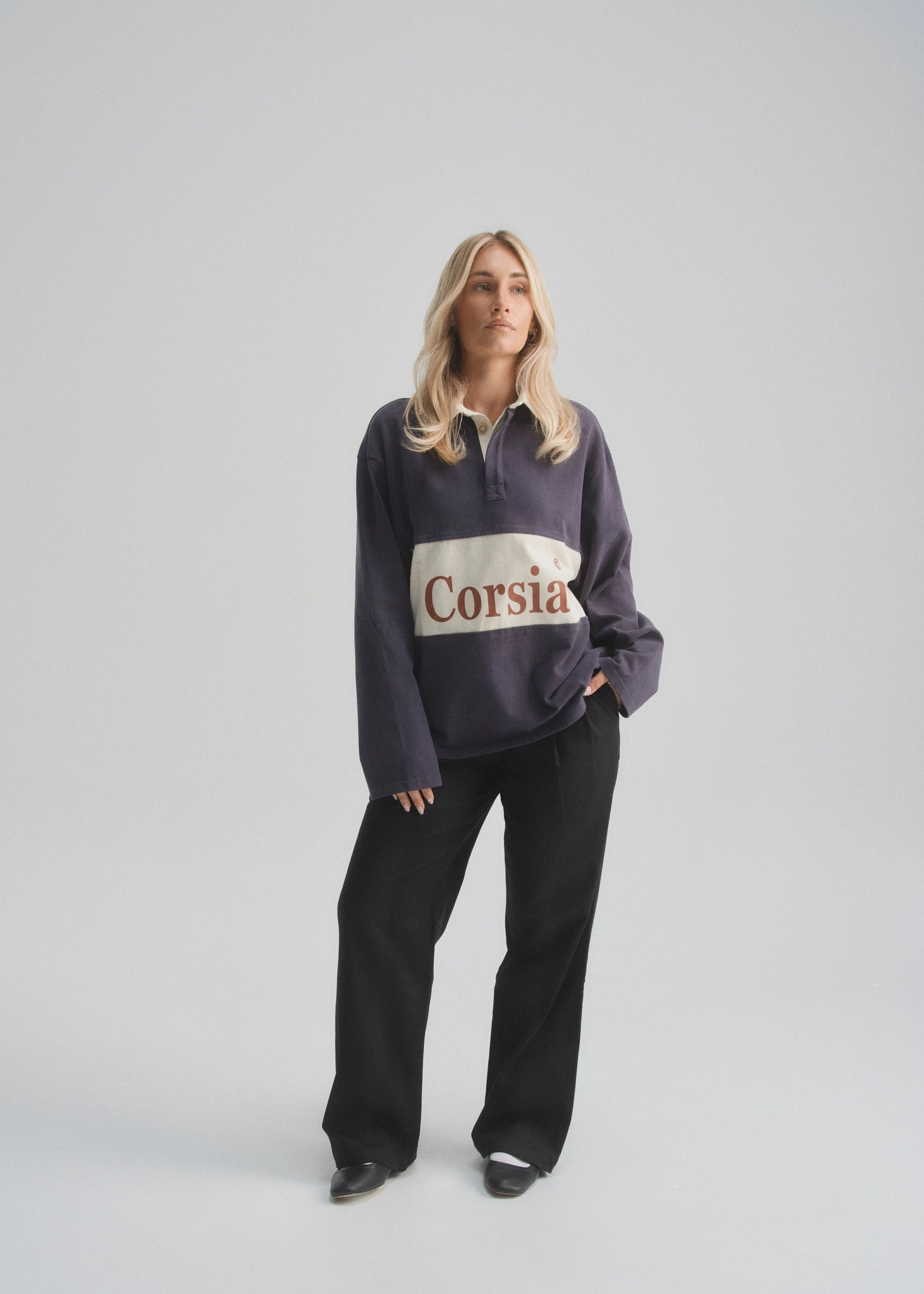 Person wearing a dark faded navy sweatshirt with 'Corsia' logo on a light gray background