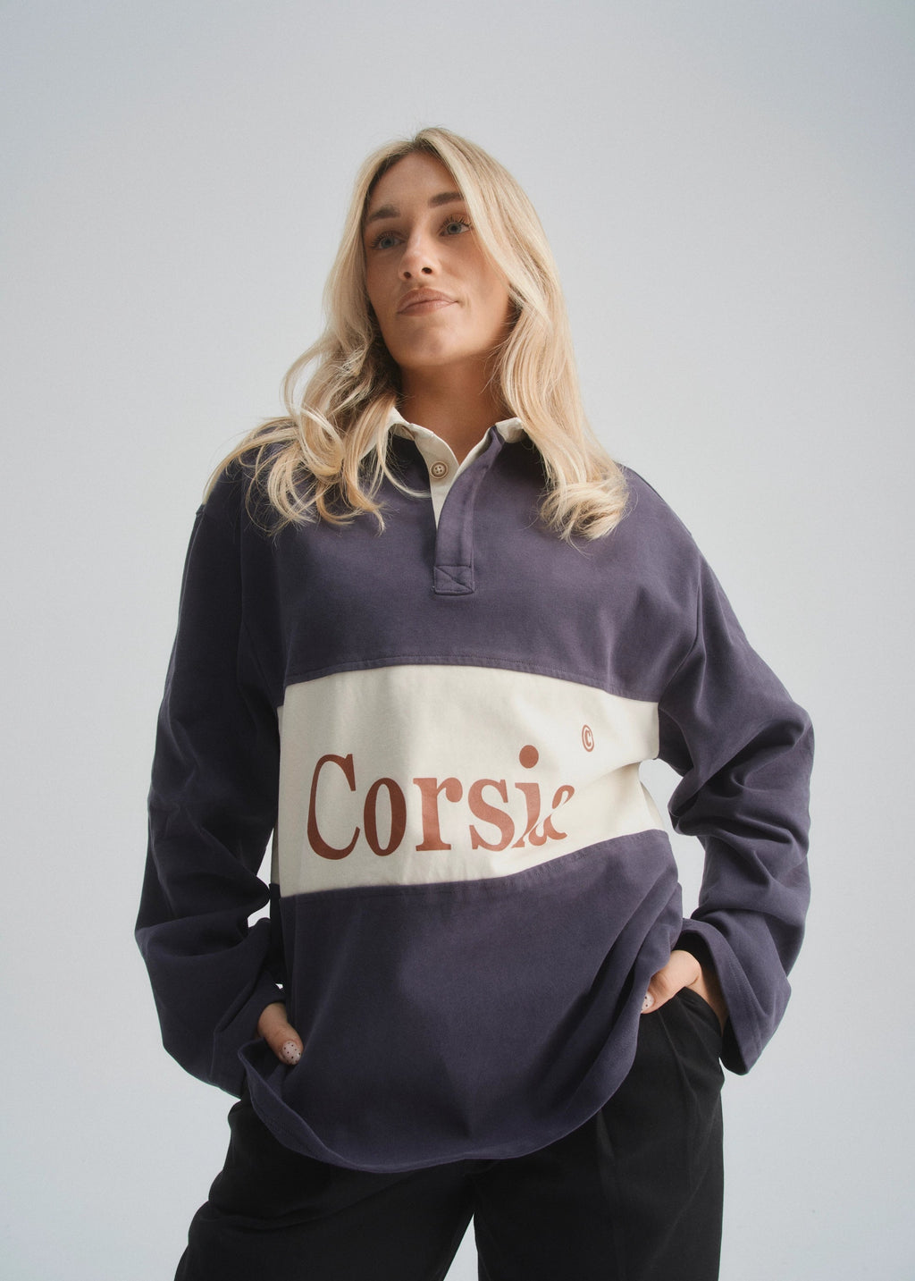 Person wearing a faded navy rugby-style shirt with 'Corsia' logo on a plain background