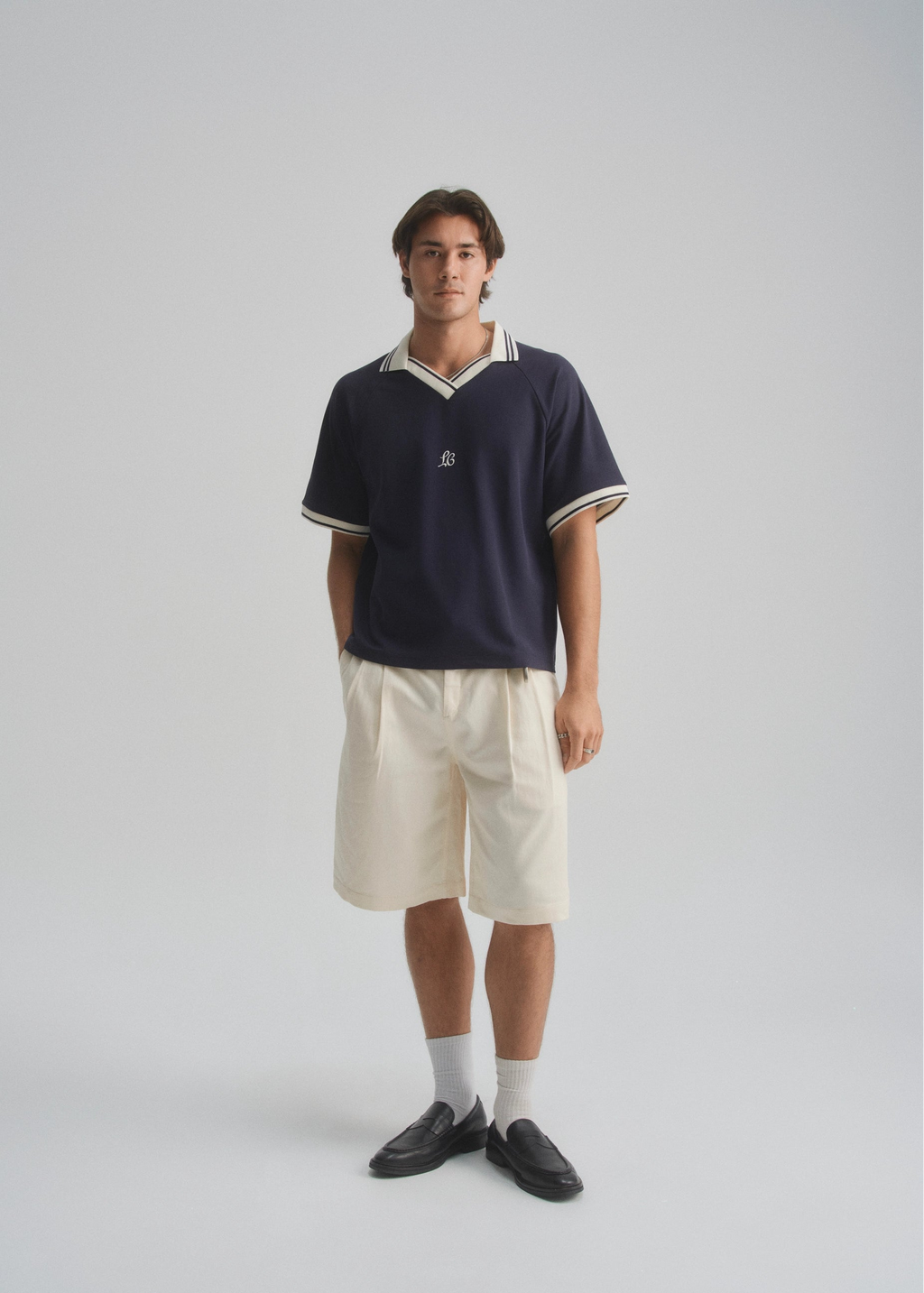 Person wearing a navy polo shirt and beige shorts on a gray background