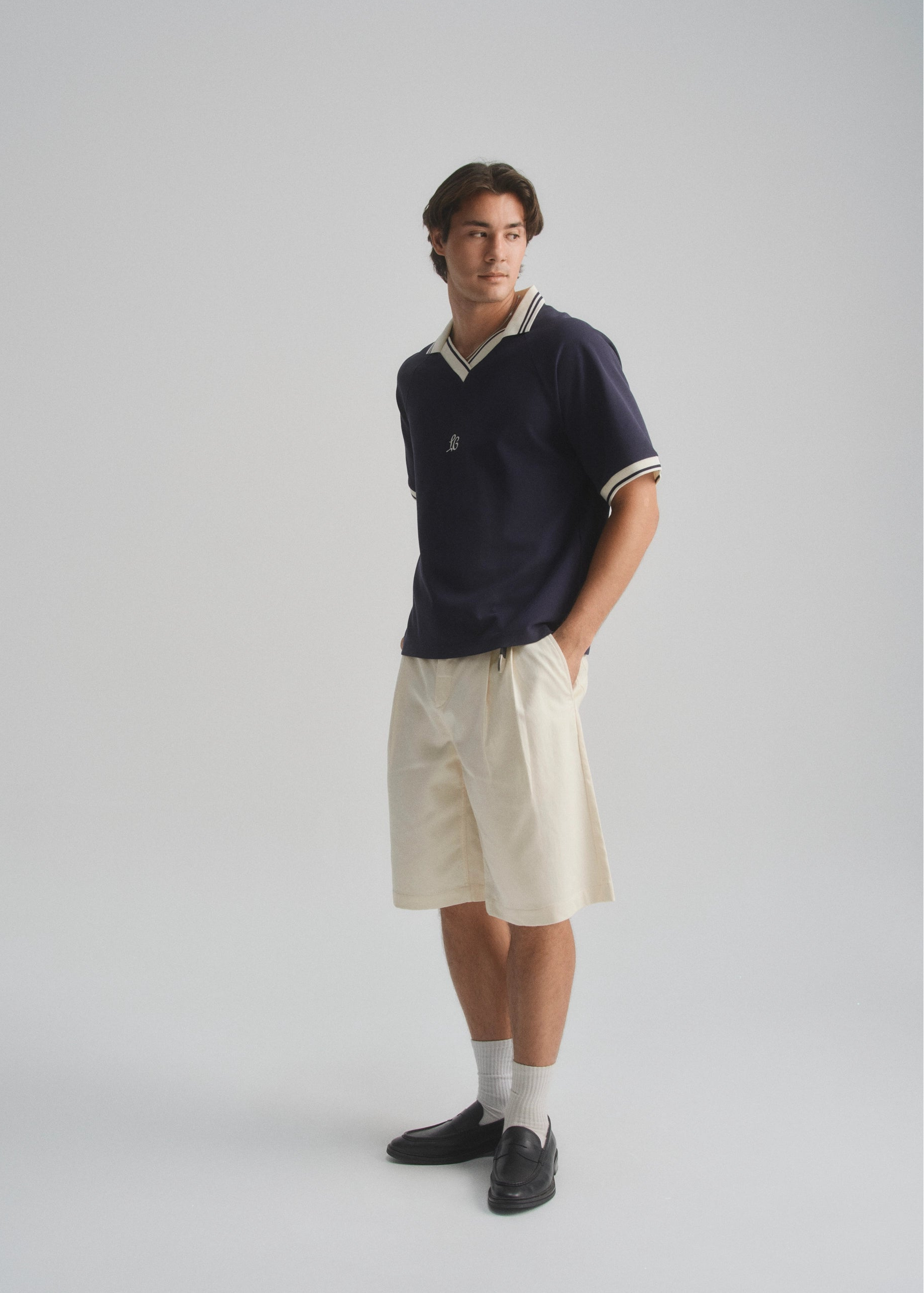 Person wearing a navy polo shirt, beige shorts, and black shoes on a plain background