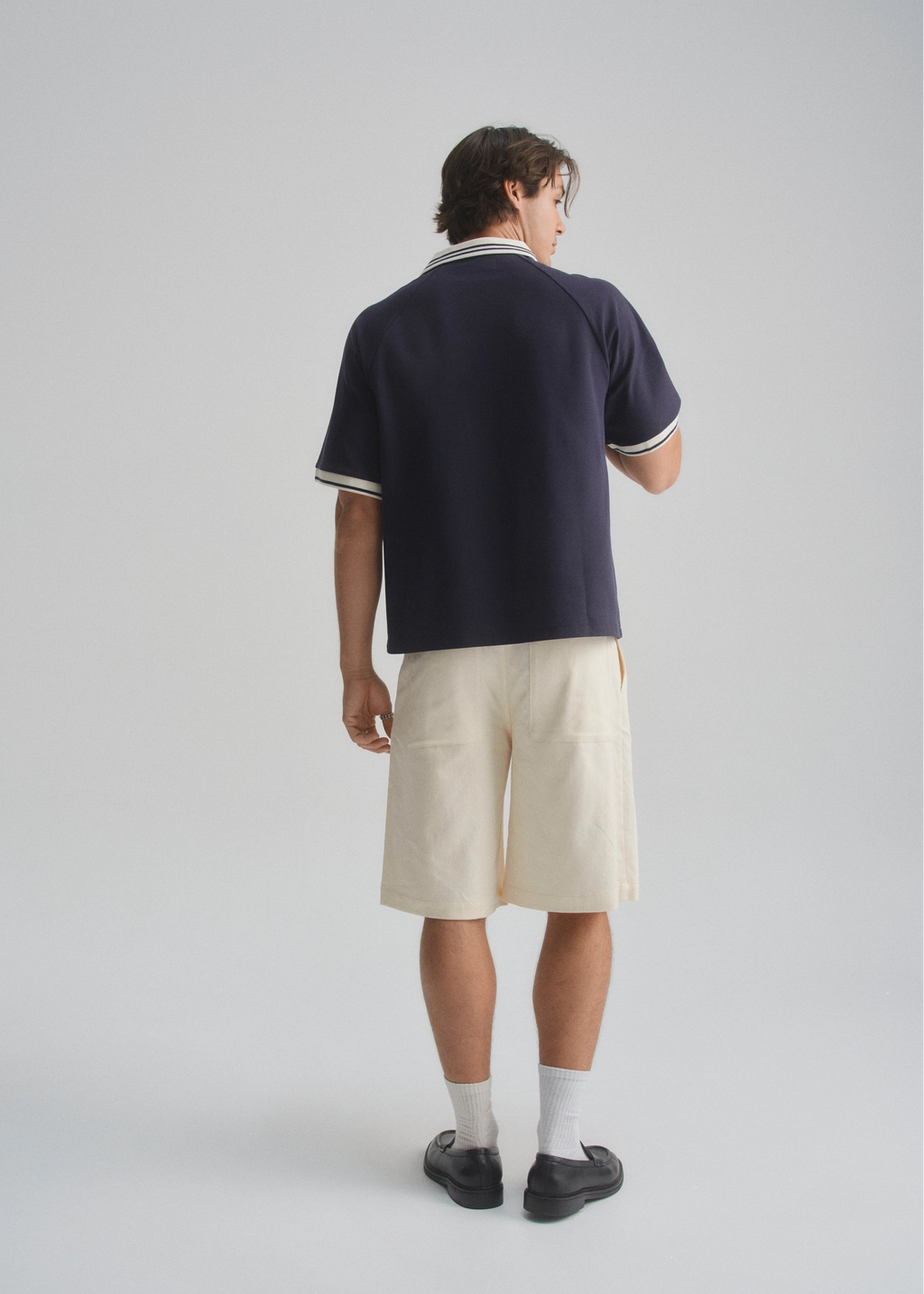 Person wearing a navy polo shirt and beige shorts on a white background